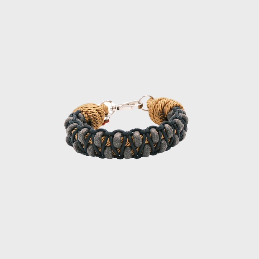 A braided macramé bracelet with shades of grey, black and yellow. It ends and a silver clasp, shown on a light gray background.
