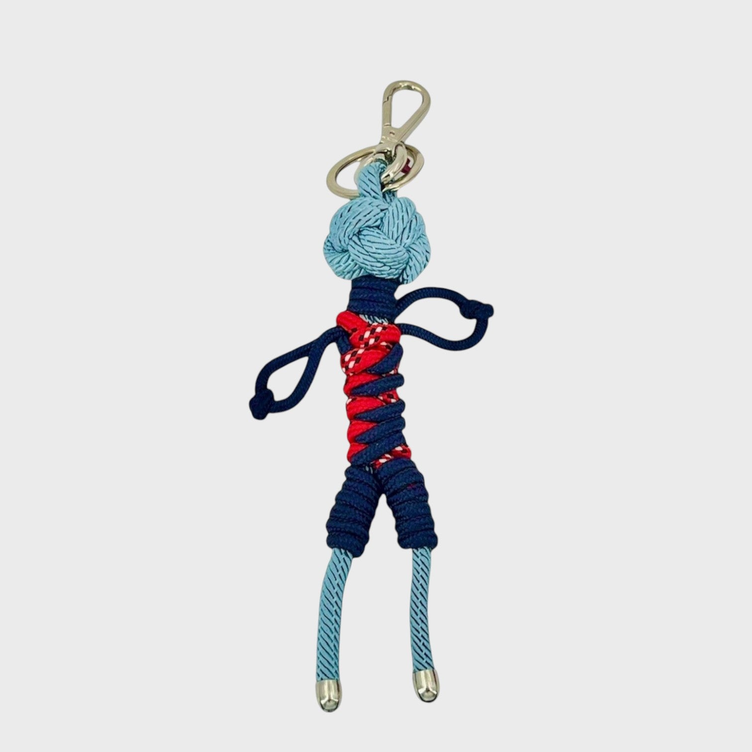 Handmade blue macramé bag charm featuring a male character, wearing short blue and red overalls. He is attached to a silver clasp.