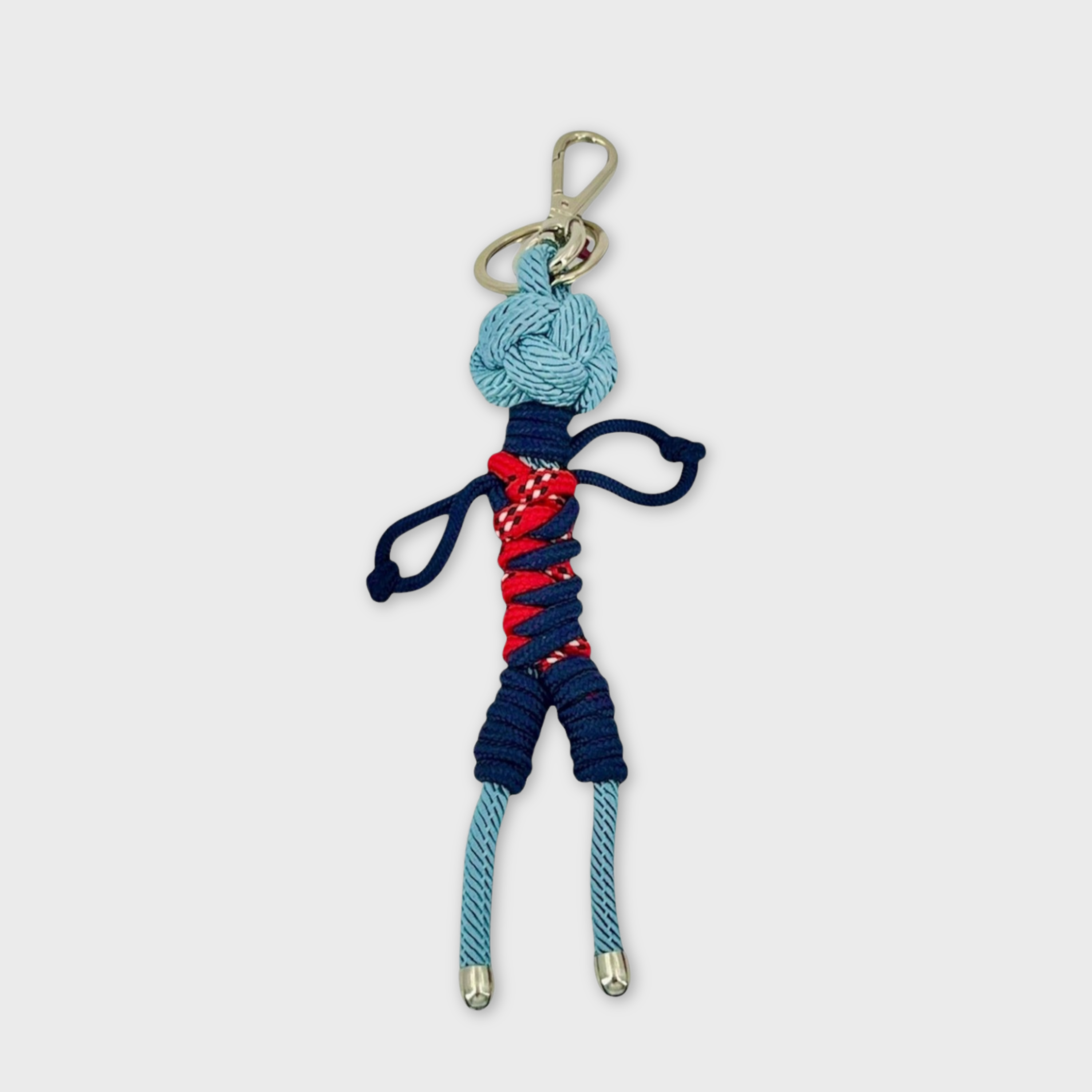 Handmade blue macramé bag charm featuring a male character, wearing short blue and red overalls. He is attached to a silver clasp.