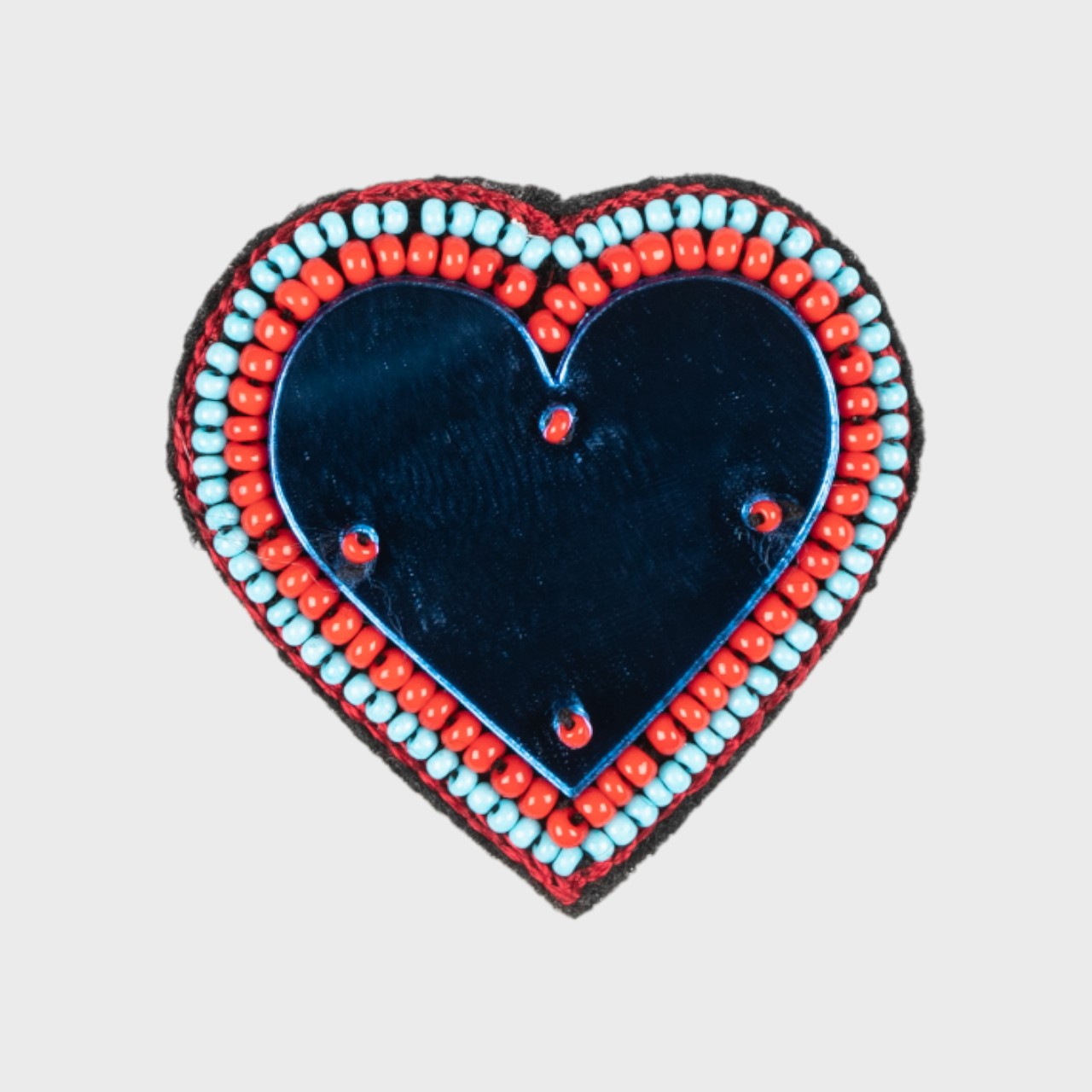 An embroidered brooch representing a heart with a blue glass middle and orange and light blue details. 