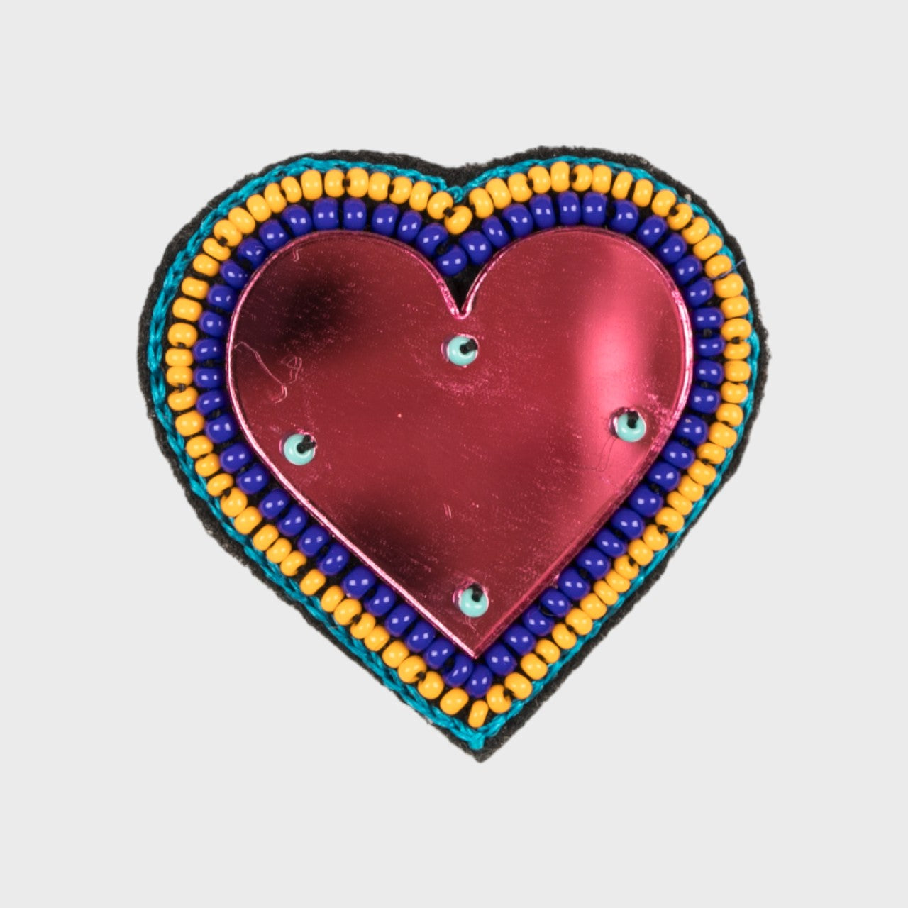 An embroidered brooch representing a heart with a pink glass center and blue and yellow details. 