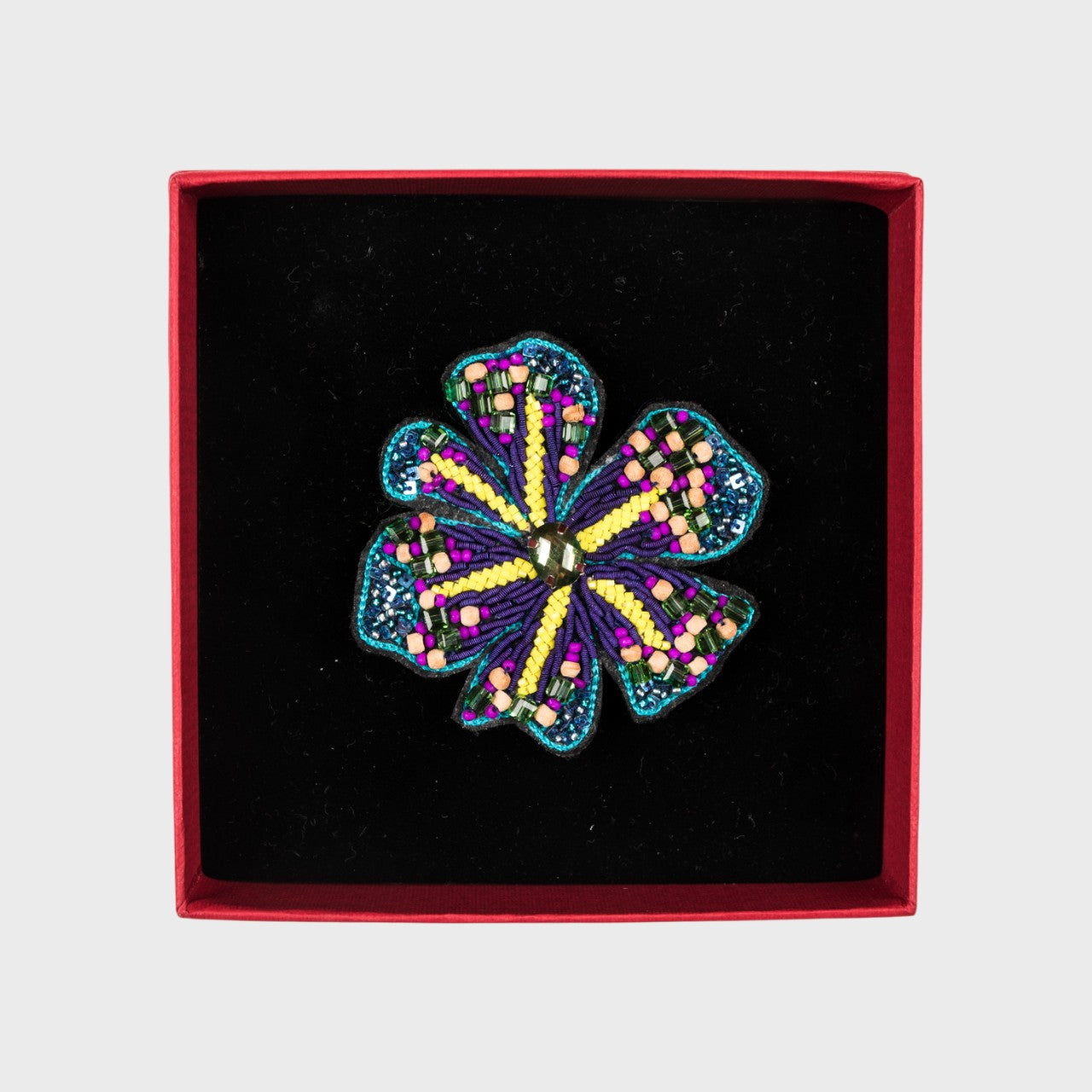 An embroidered brooch with blue, purple and yellow details in a box. 