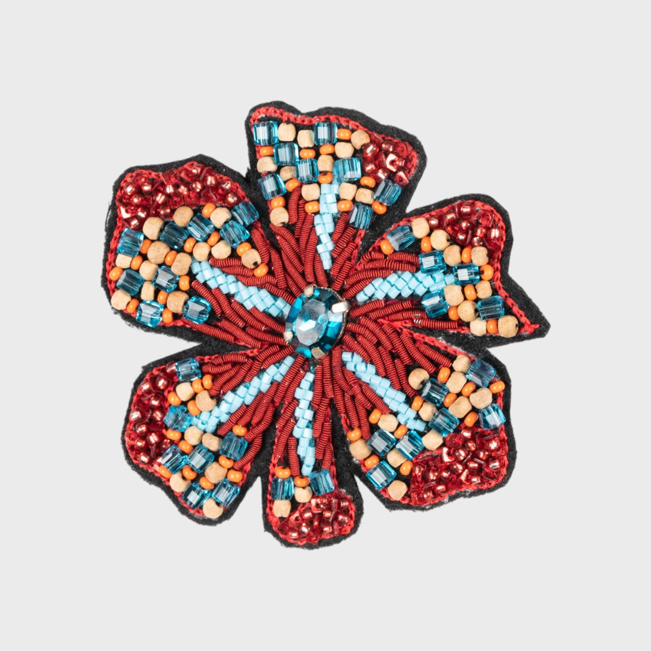 An embroidered brooch representing a flower with red, blue and beige details. 