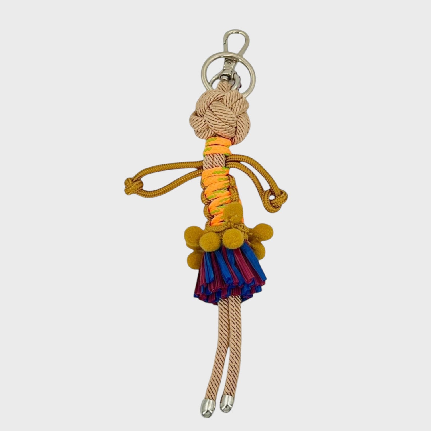 Handmade macramé bag charm featuring an exotic character wearing a short blue and red fringed skirt and a fun mustard yellow belt. She is attached to a silver clasp.