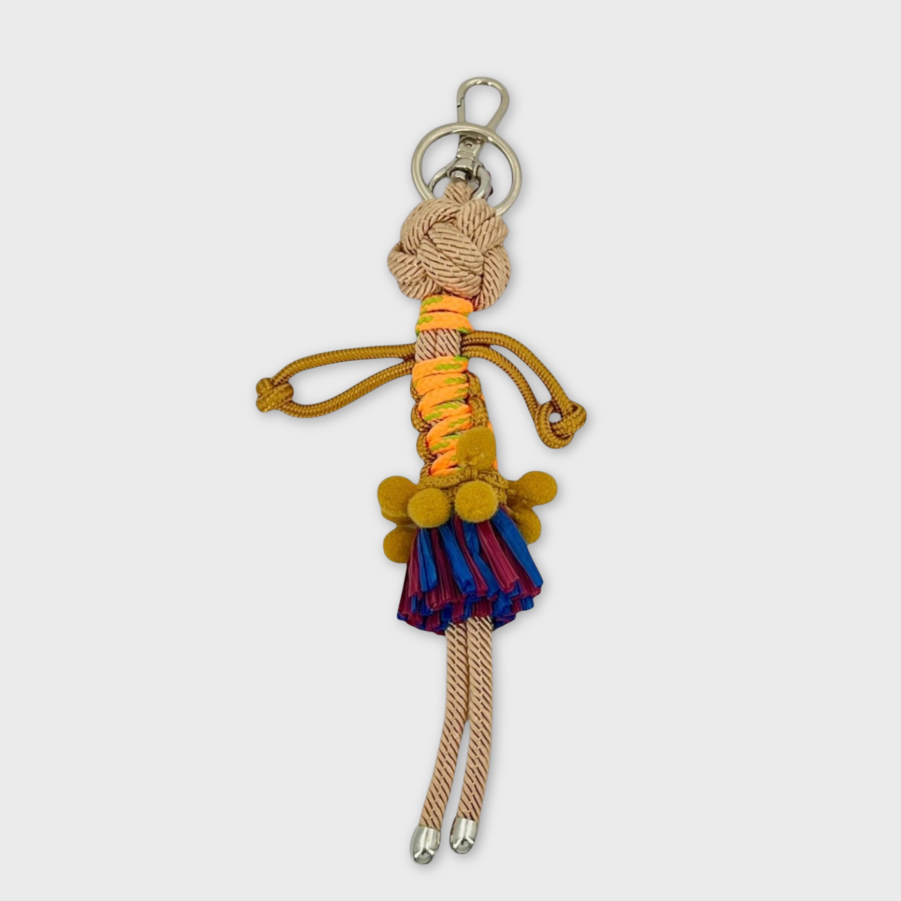 Handmade macramé bag charm featuring an exotic character wearing a short blue and red fringed skirt and a fun mustard yellow belt. She is attached to a silver clasp.
