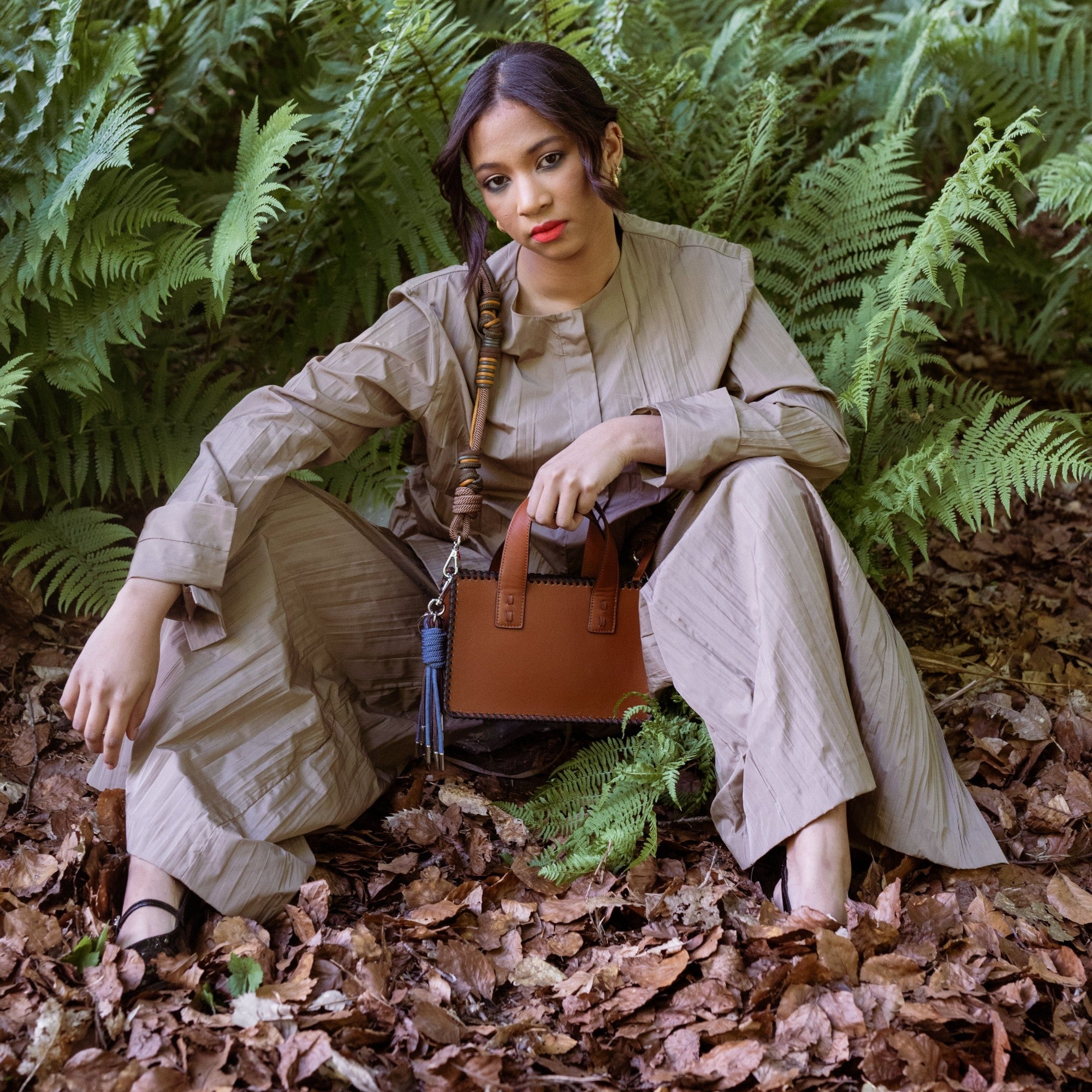 A model sitting carrying by the yellow and green strap the brown leather Maori Handbag. 