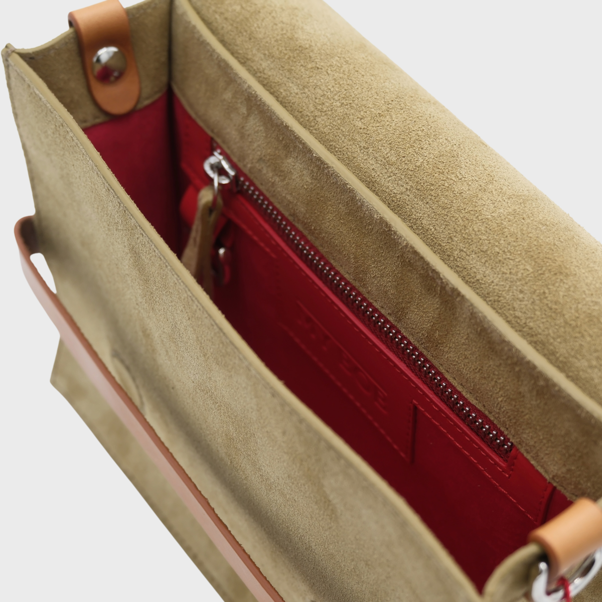 Close-up of a green suede bag interior showing a red zippered pocket and red lining, with tan leather trim and a silver zipper pull.