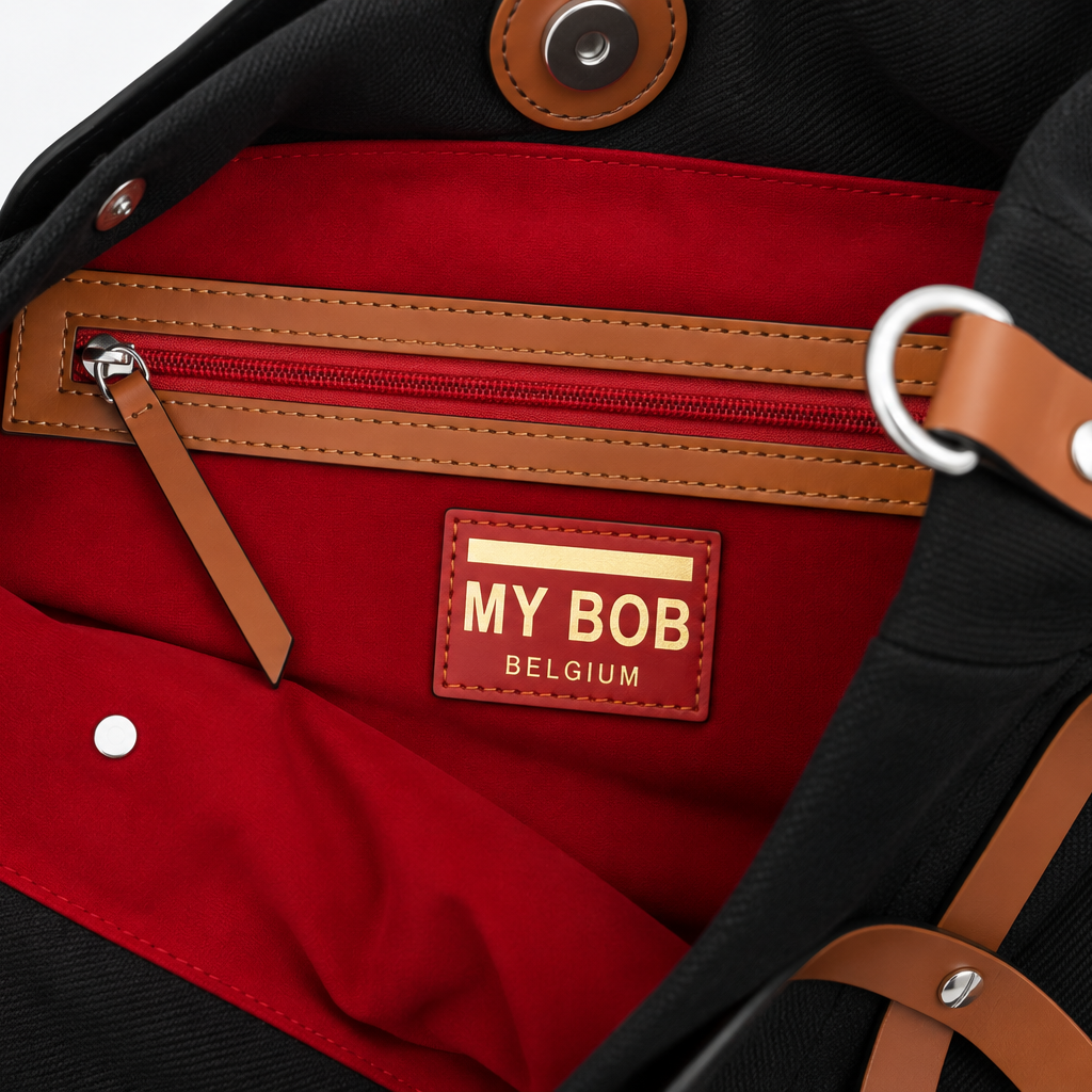Close-up of the interior of a black canvas tote bag with a bright red velvet lining, tan leather trim, and a central label reading 'MY BOB BELGIUM'.