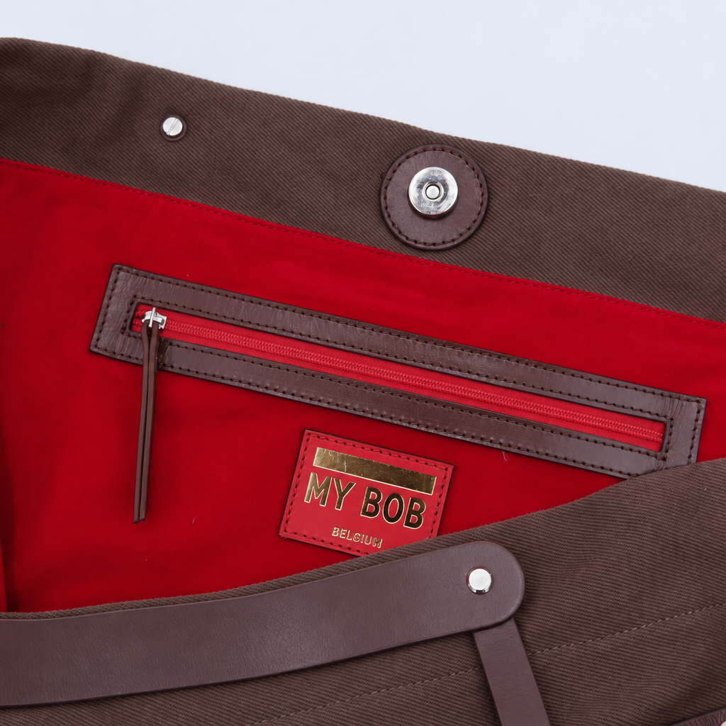 Close-up of the interior of a brown cotton canvas bag with a bright red lining, a zippered pocket, and a visible MY BOB brand patch.