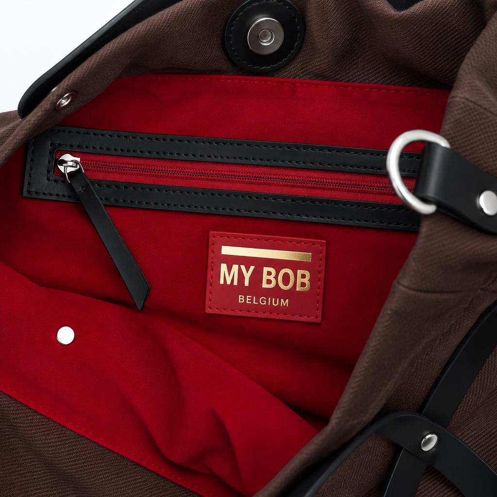 Close-up of a brown bag's interior showing a red fabric lining, a black zipper pocket, and a red leather patch with the brand name 'MY BOB BELGIUM'.