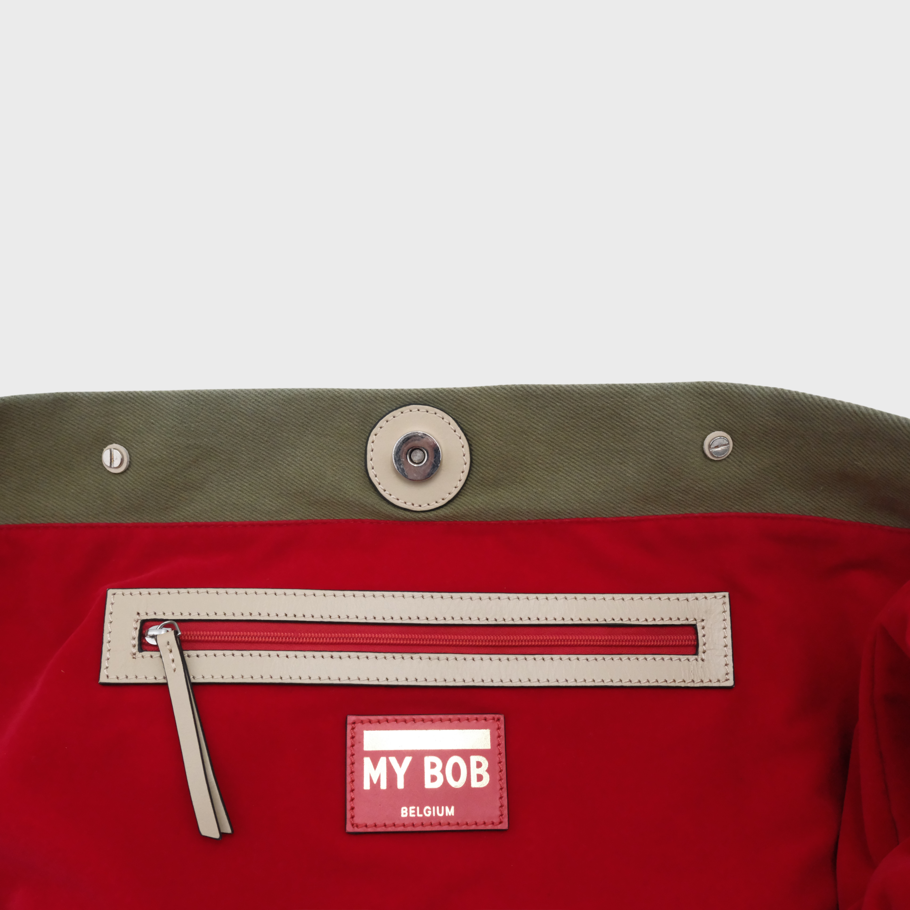 Close-up of the red inside of the olive green Candide in canvas. Showing the red zipper with light leather contour to match the harness at the front leading to the small inside pocket of the weekender bag.