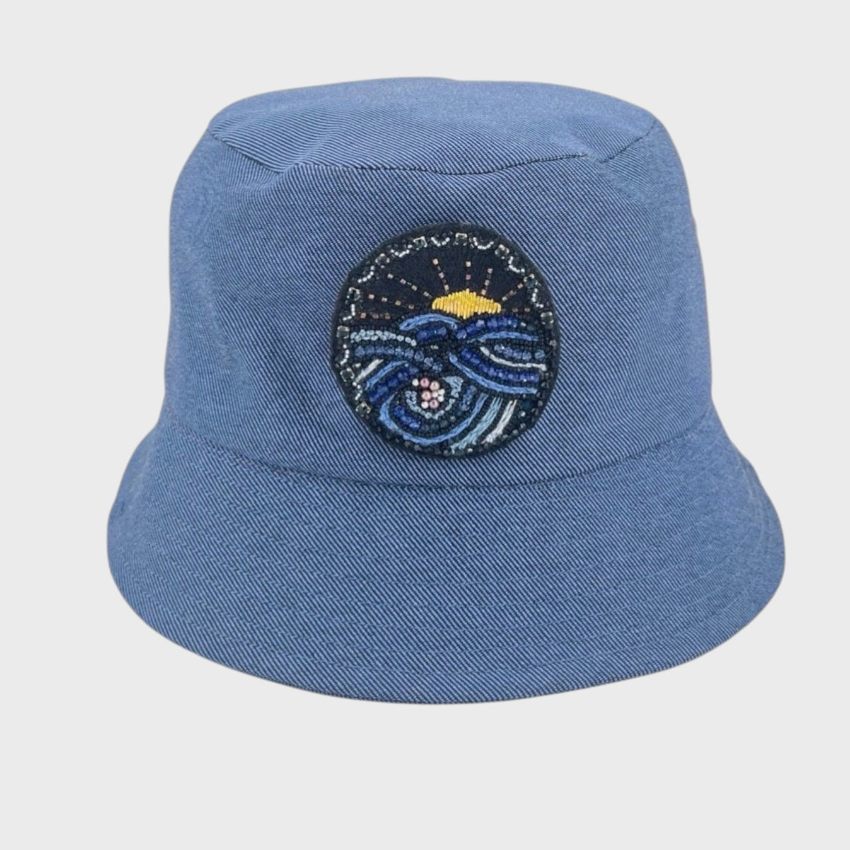 Blue jean bucket hat with an embroidered brooch on a light gray background