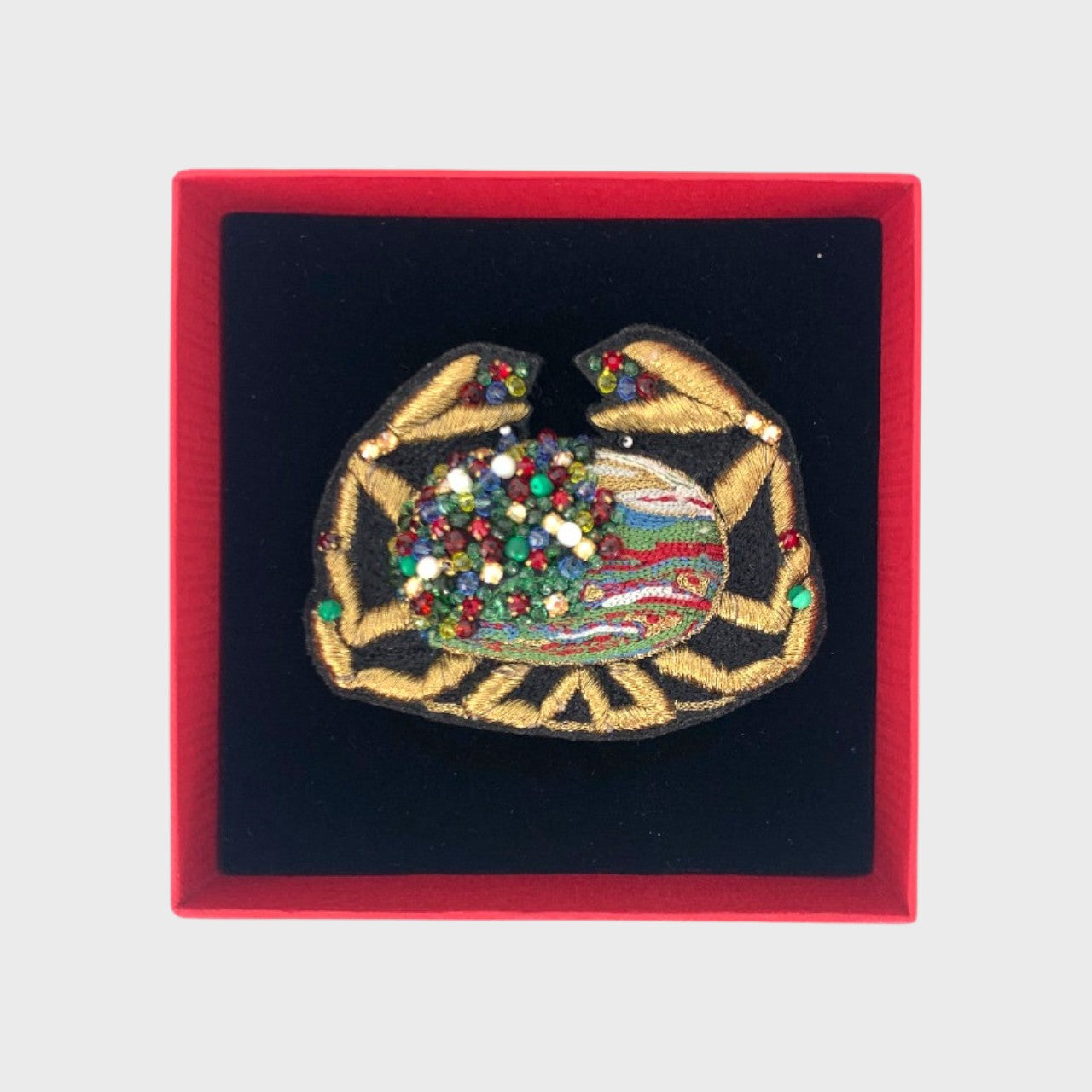 An embroidered brooch represeting a crab in a box. 