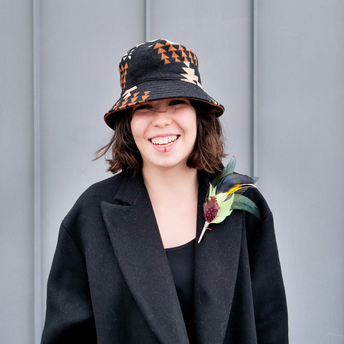 A woman wearing a black coat, adorned with a colorful feather brooch pinned to her lapel.