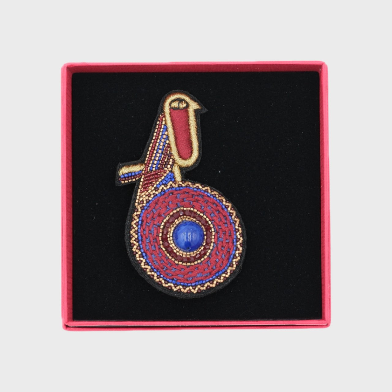 An embroidered brooch representing a purple kiwi bird in a box. 