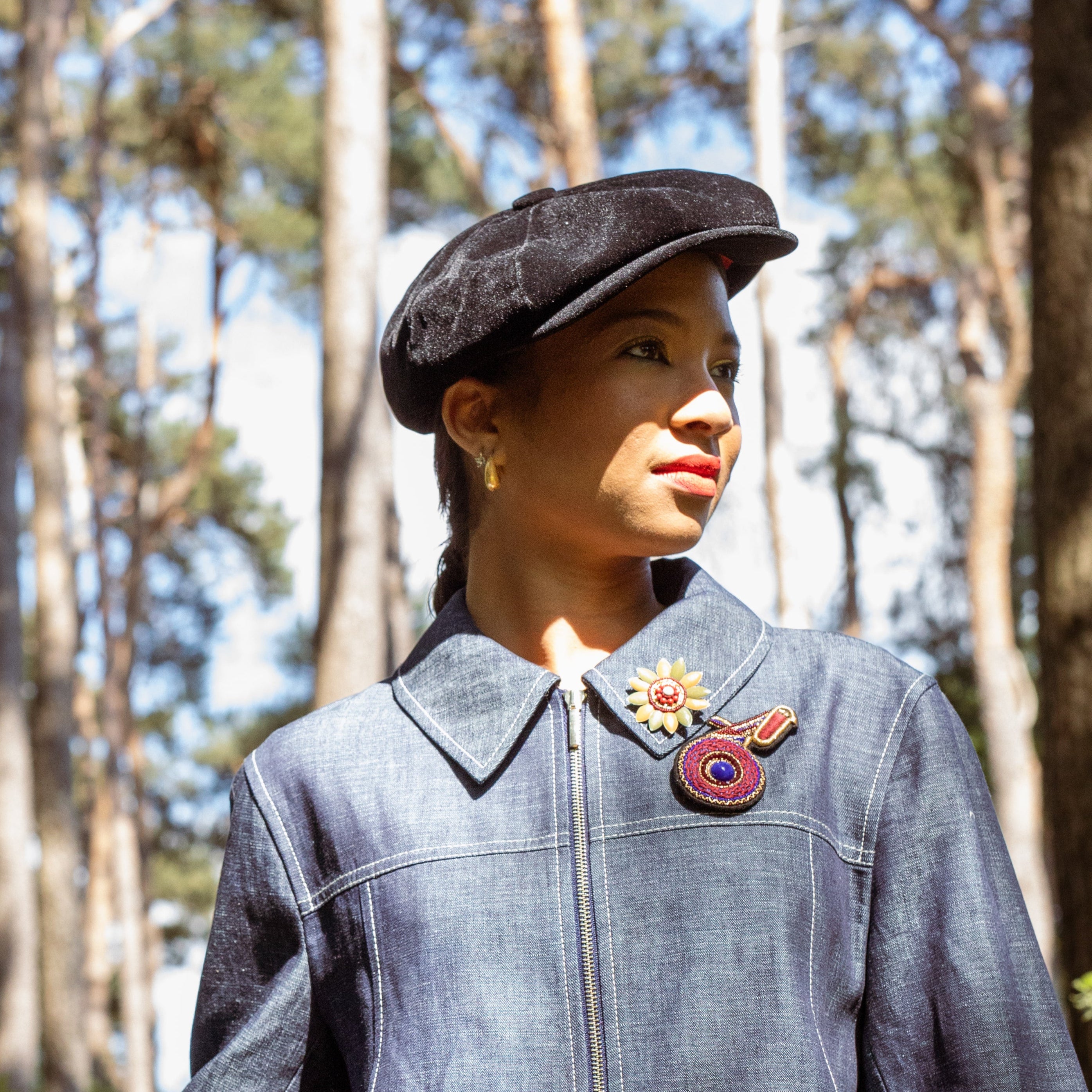 An embroidered brooch representing a purple kiwi brooch worn by a model. 