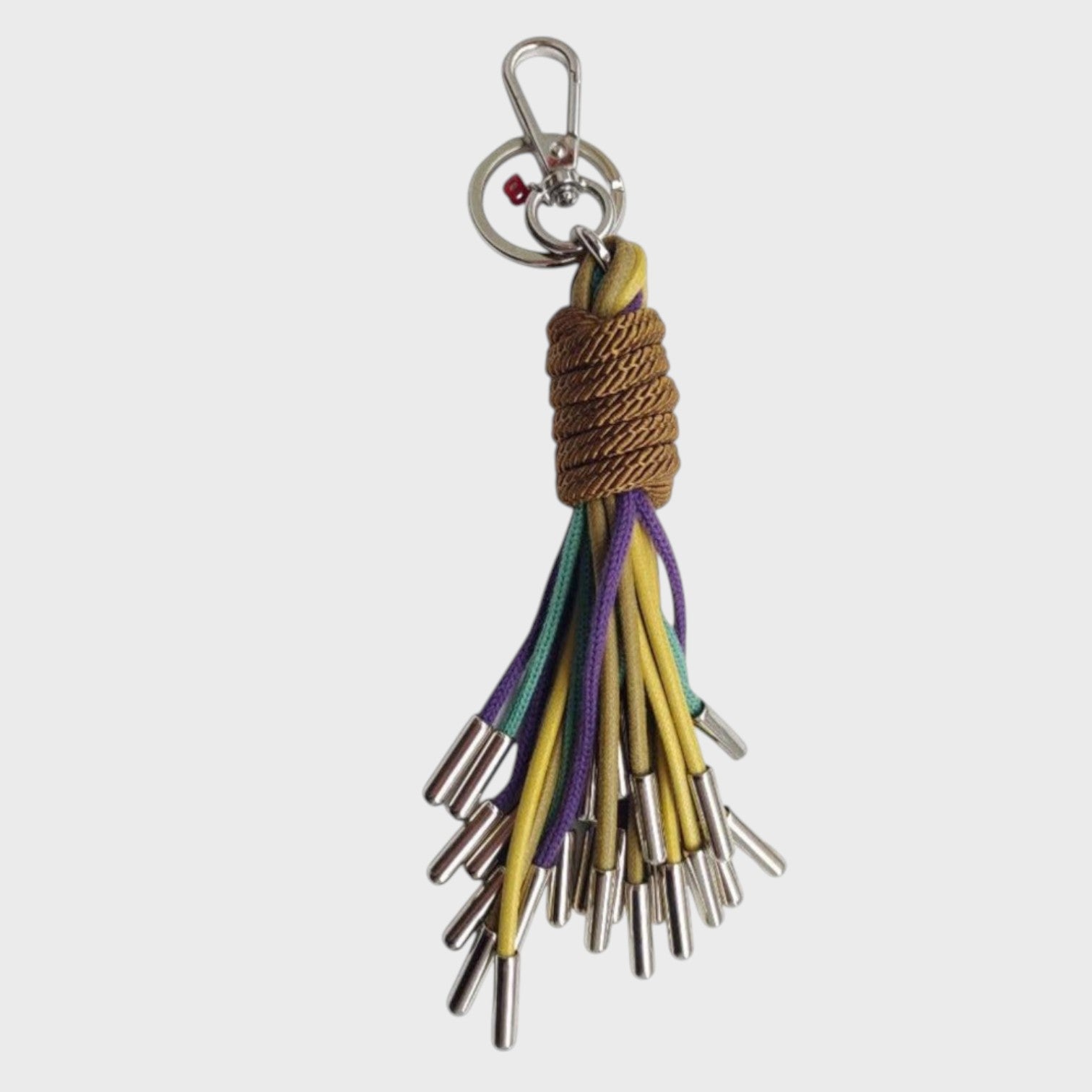 A keychain tassel with a silver metal clasp and ring, featuring a brown woven wrap and multiple hanging cords in yellow, purple, and blue.