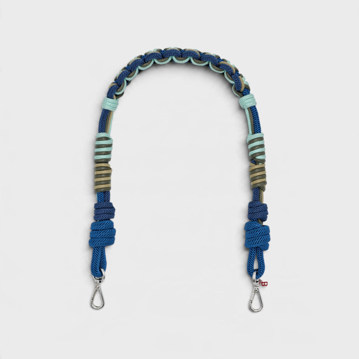 Multicolored braided macramé bag strap in bright blue, dark blue, and green with metal hooks on a light gray background.