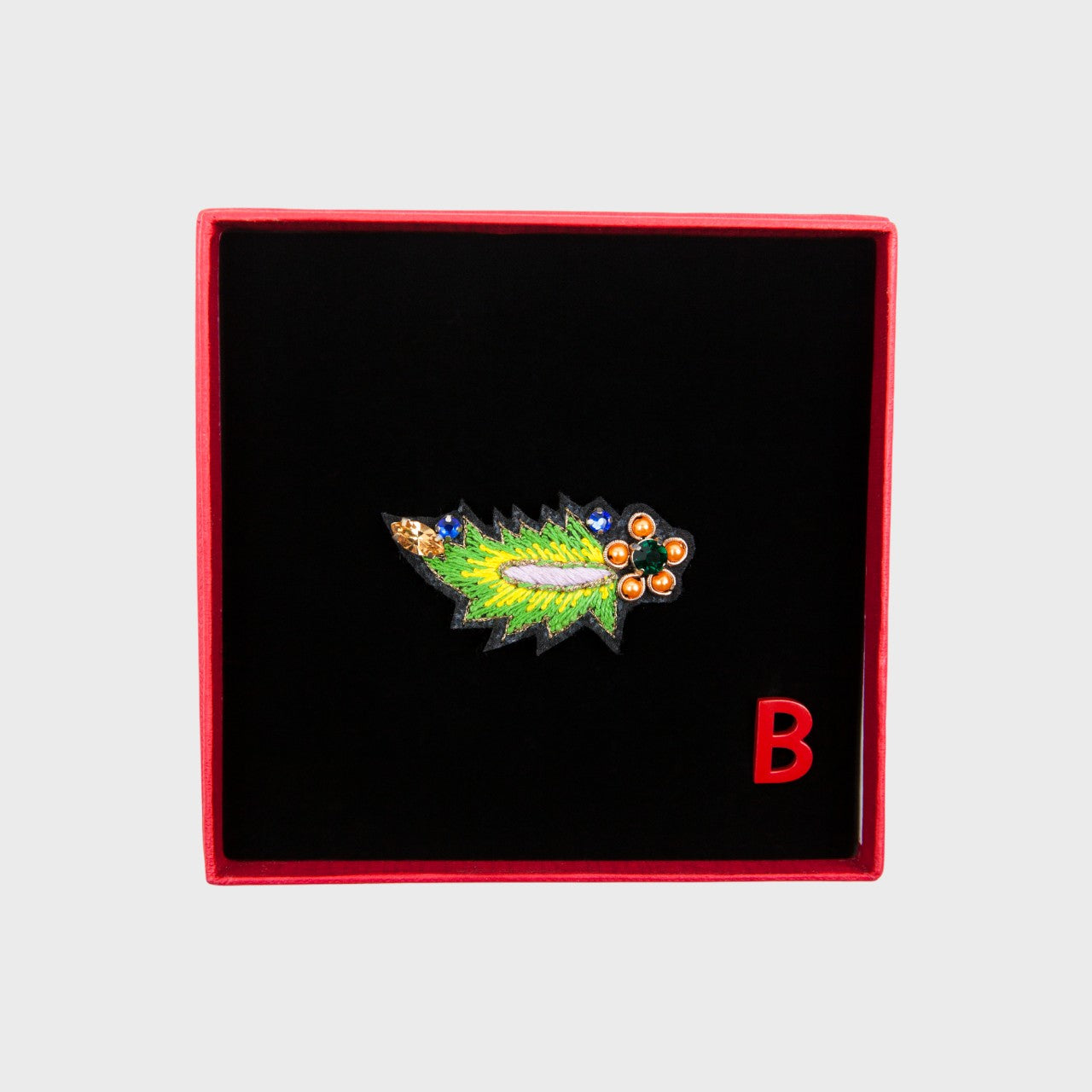 An embroidered brooch representing a green leaf in a box. 
