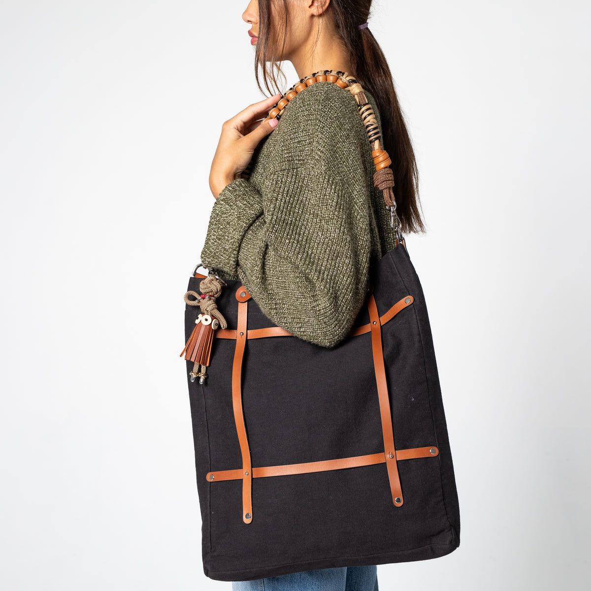 Person holding a black bag with brown macramé and leather straps against a white background