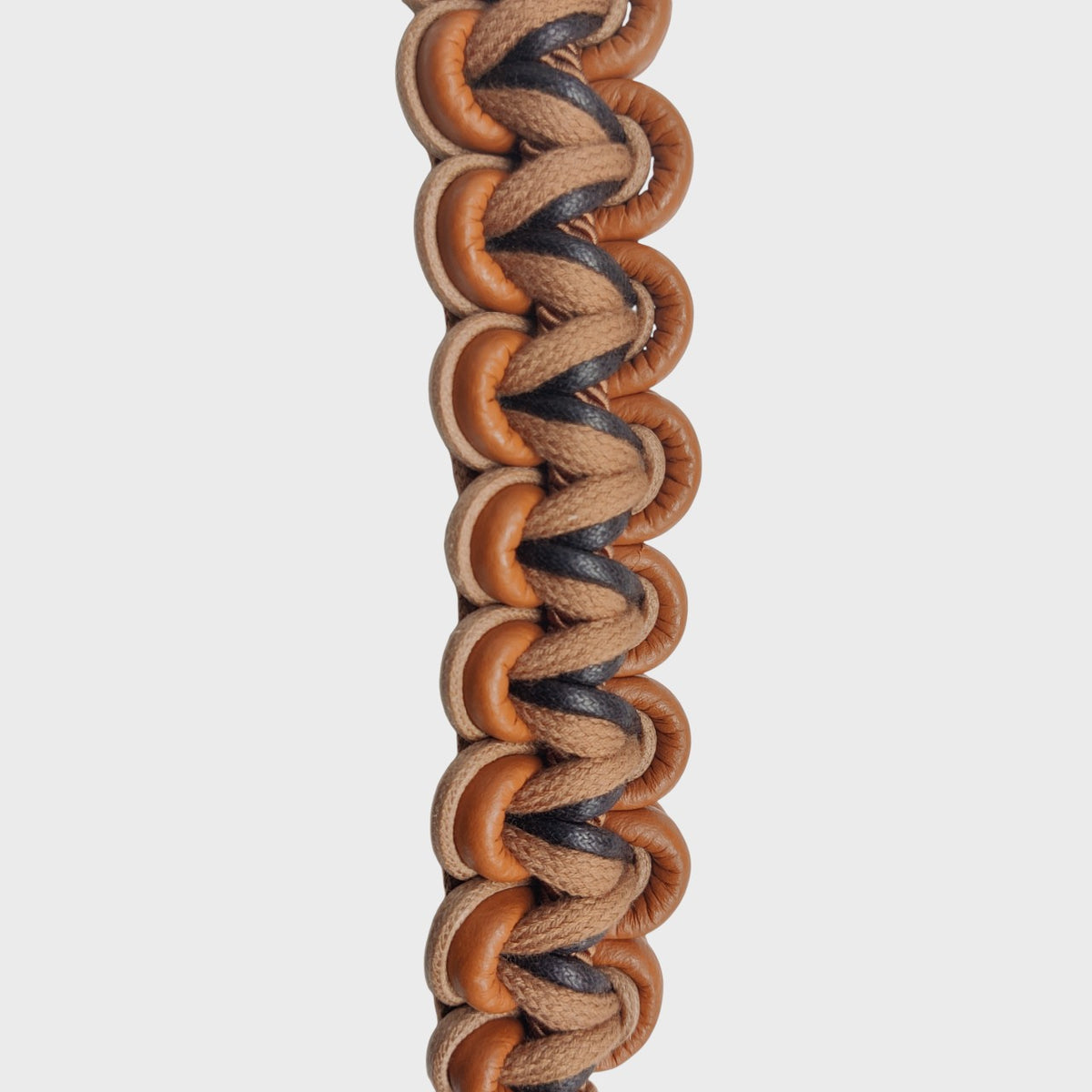 The detail of a braided brown bag strap with macramé and leather. 