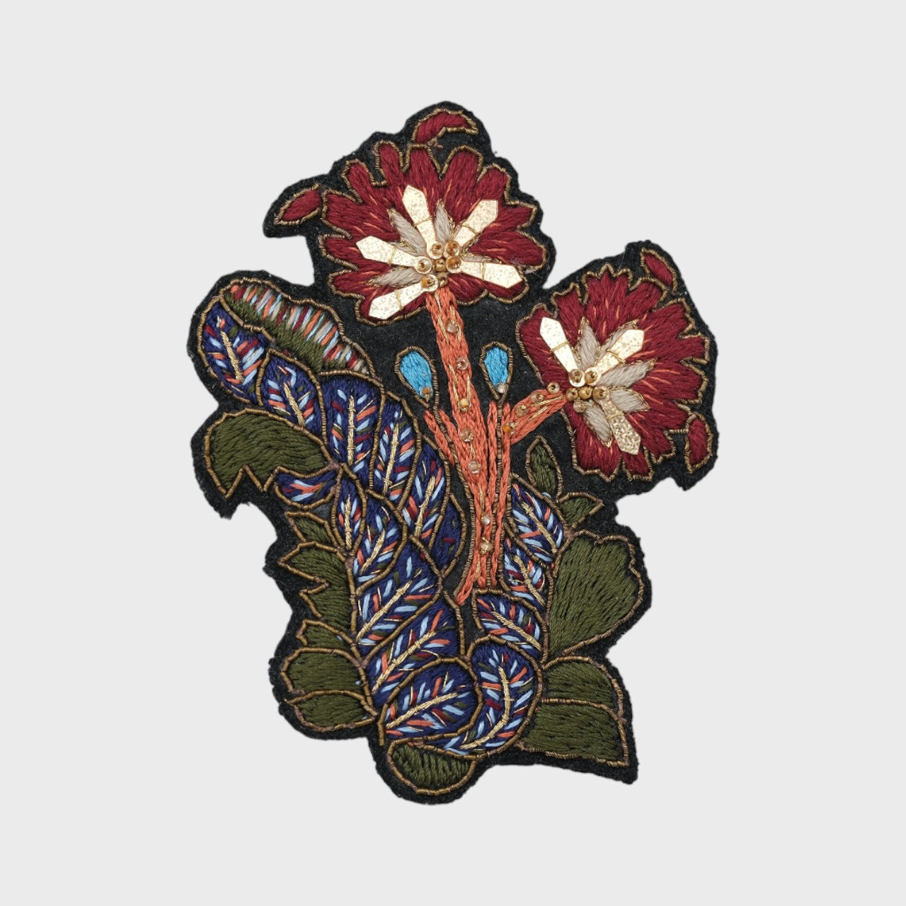 An embroidered brooch representing a flower with its leaves with red, blue and green details. 