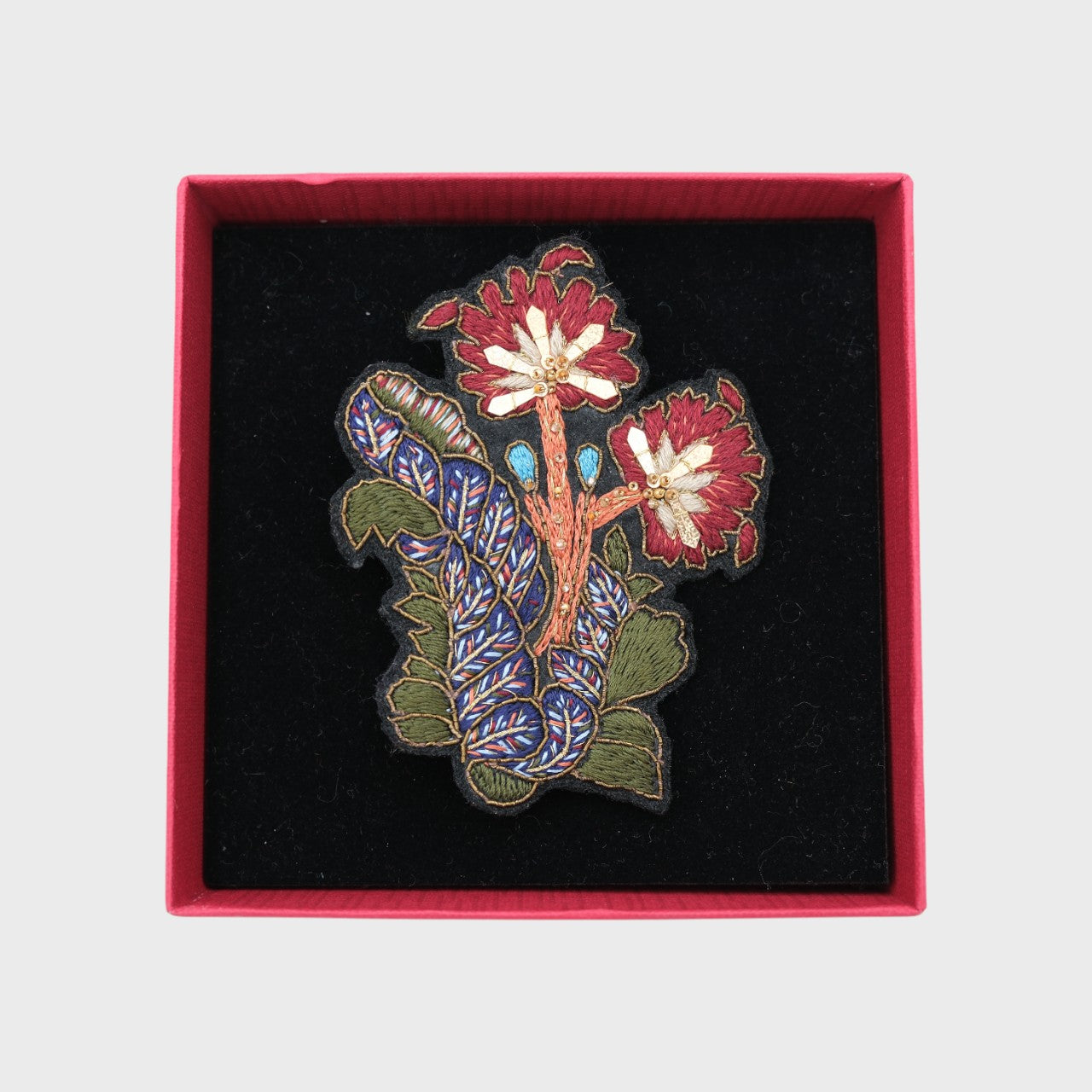 An embroidered brooch representing leaves and flowers in a box. 