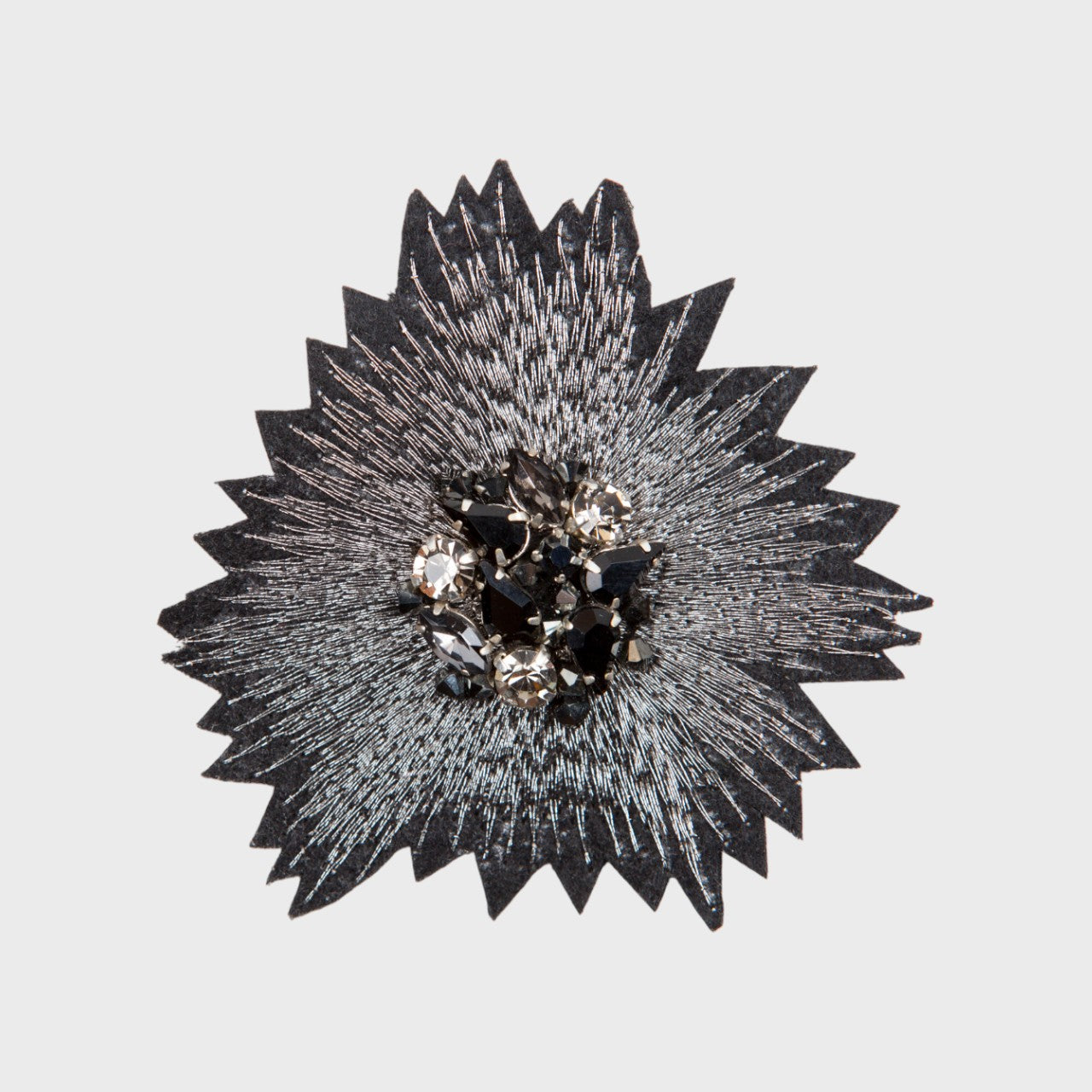 An embroidered brooch representing the silver sunset with black and white stones in the middle. 