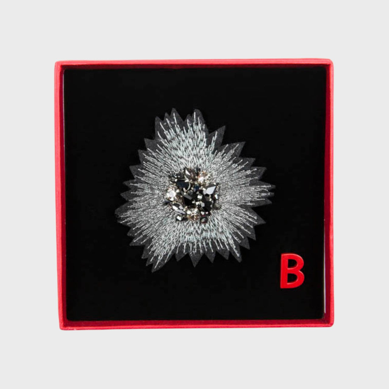 An embroidered brooch representing the silver sunset in a box. 