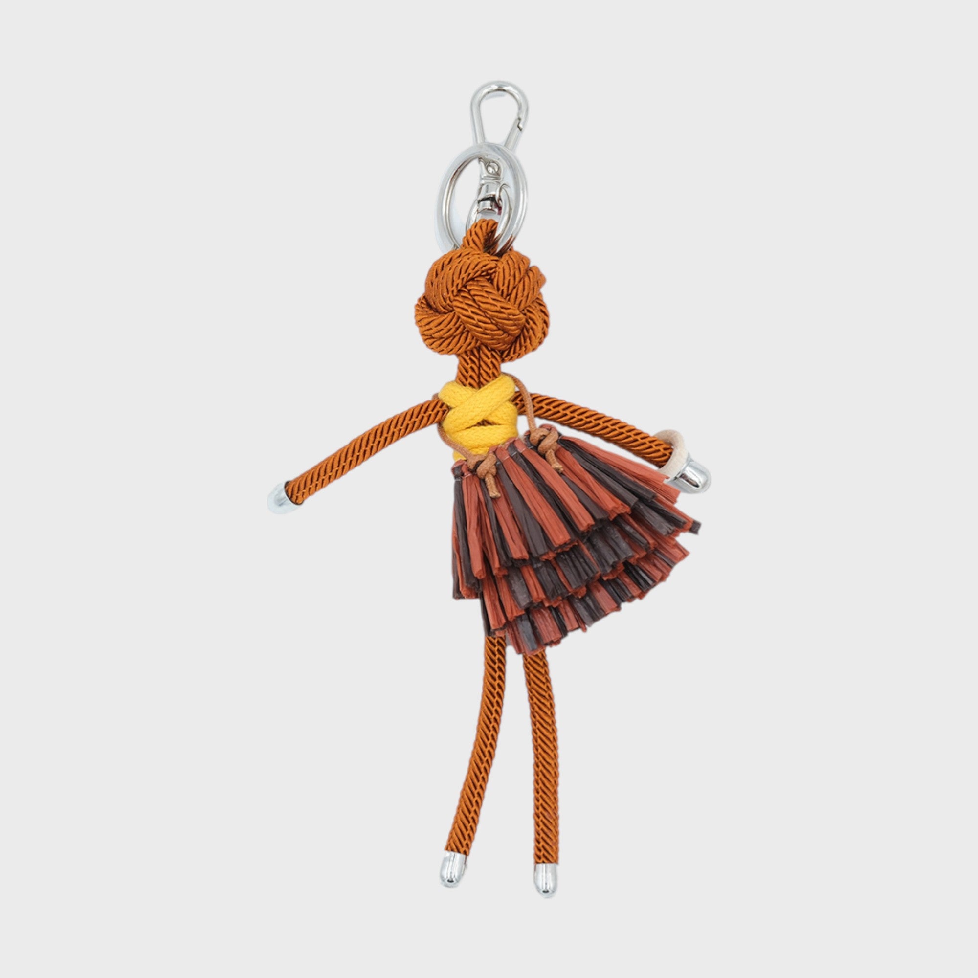 Handmade brown macramé bag charm featuring a character in a bright yellow top and layered mini skirt in various browns and a white bracelet. She is attached to a silver clasp.