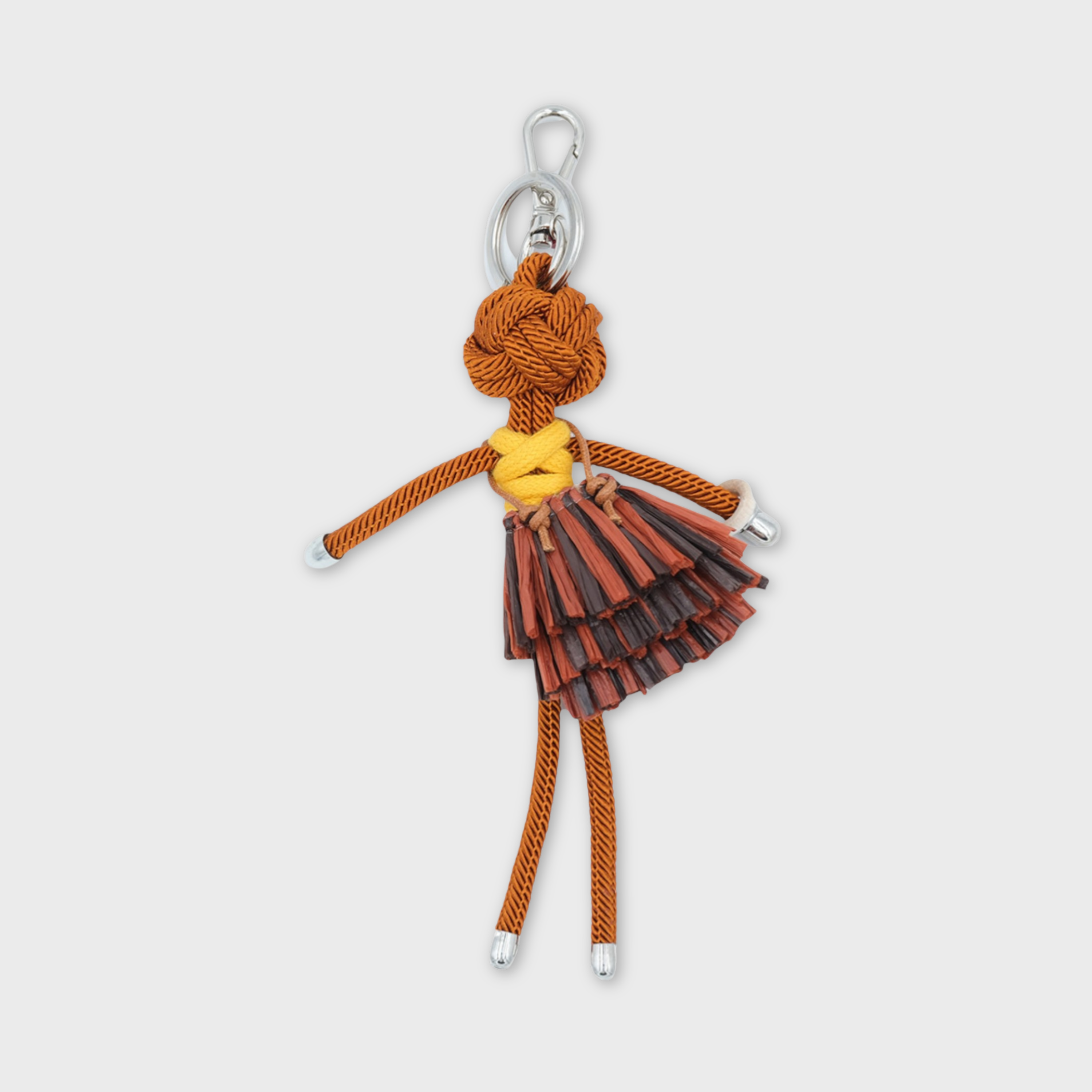 Handmade brown macramé bag charm featuring a character in a bright yellow top and layered mini skirt in various browns and a white bracelet. She is attached to a silver clasp.