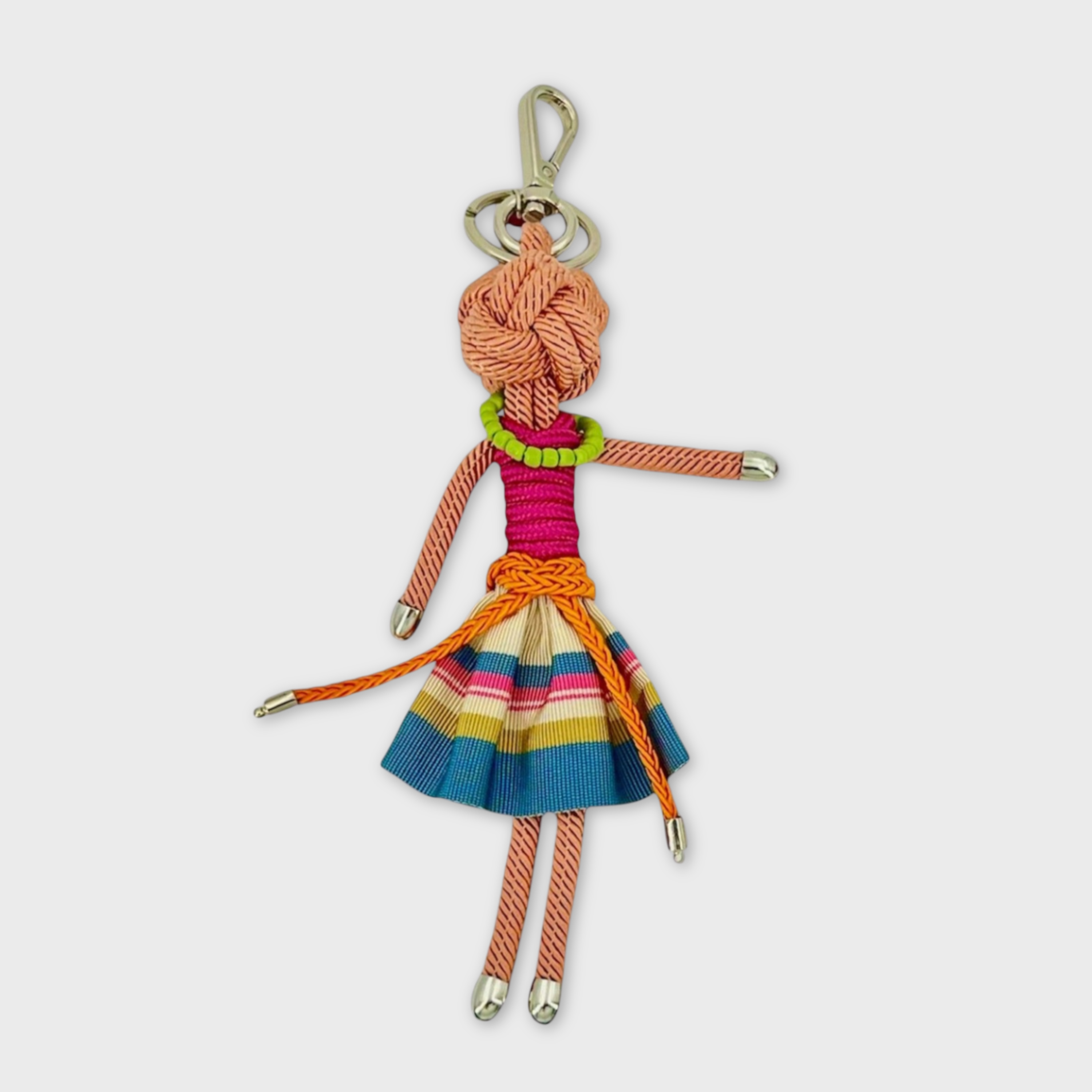 Handmade tan macramé bag charm featuring a female character, wearing a striped blue and white mini skirt paired with an orange belt, a short sleeves pink top and a green beaded necklace. She is attached to a silver clasp.