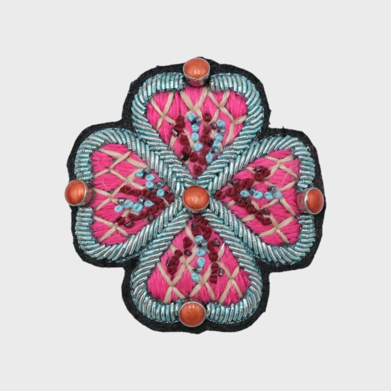 An embroidered brooch representing a pink flower with blue details. 