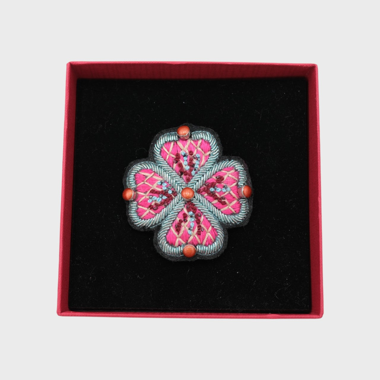 An embroidered brooch representing a pink flower in a box. 
