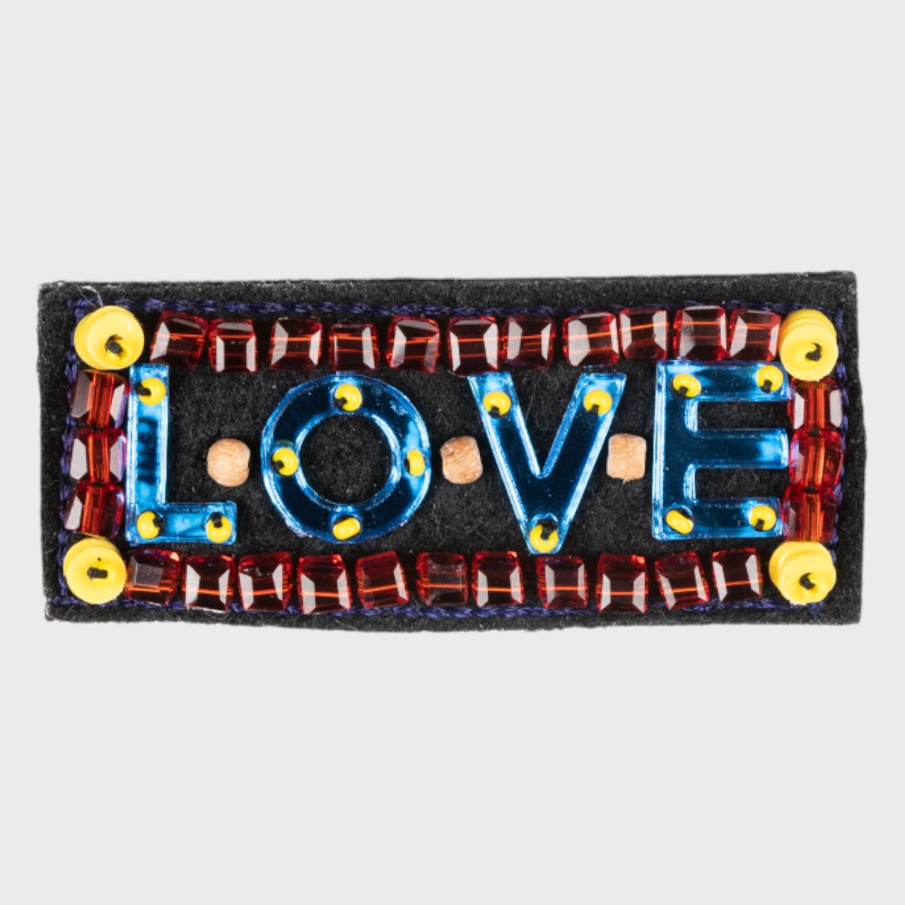 An embroidered blue brooch with LOVE in the middle and red details. 
