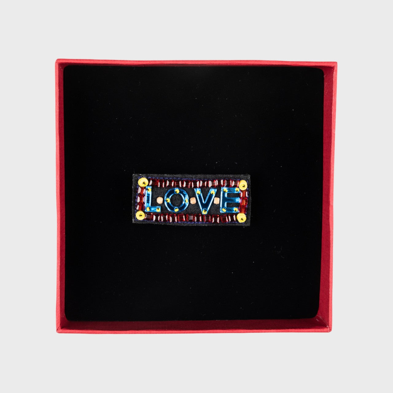 An embroidered brooch in blue and red with LOVE in a box. 