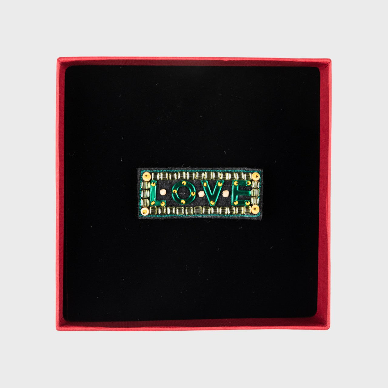 An embroidered green brooch with written LOVE in a box. 