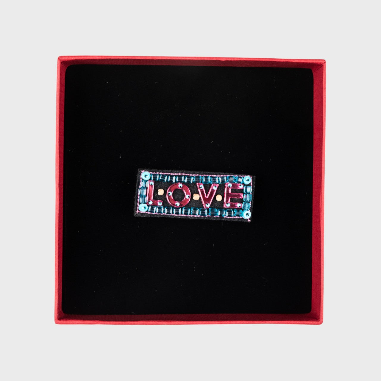An embroidered pink brooch with written LOVE, in a box. 
