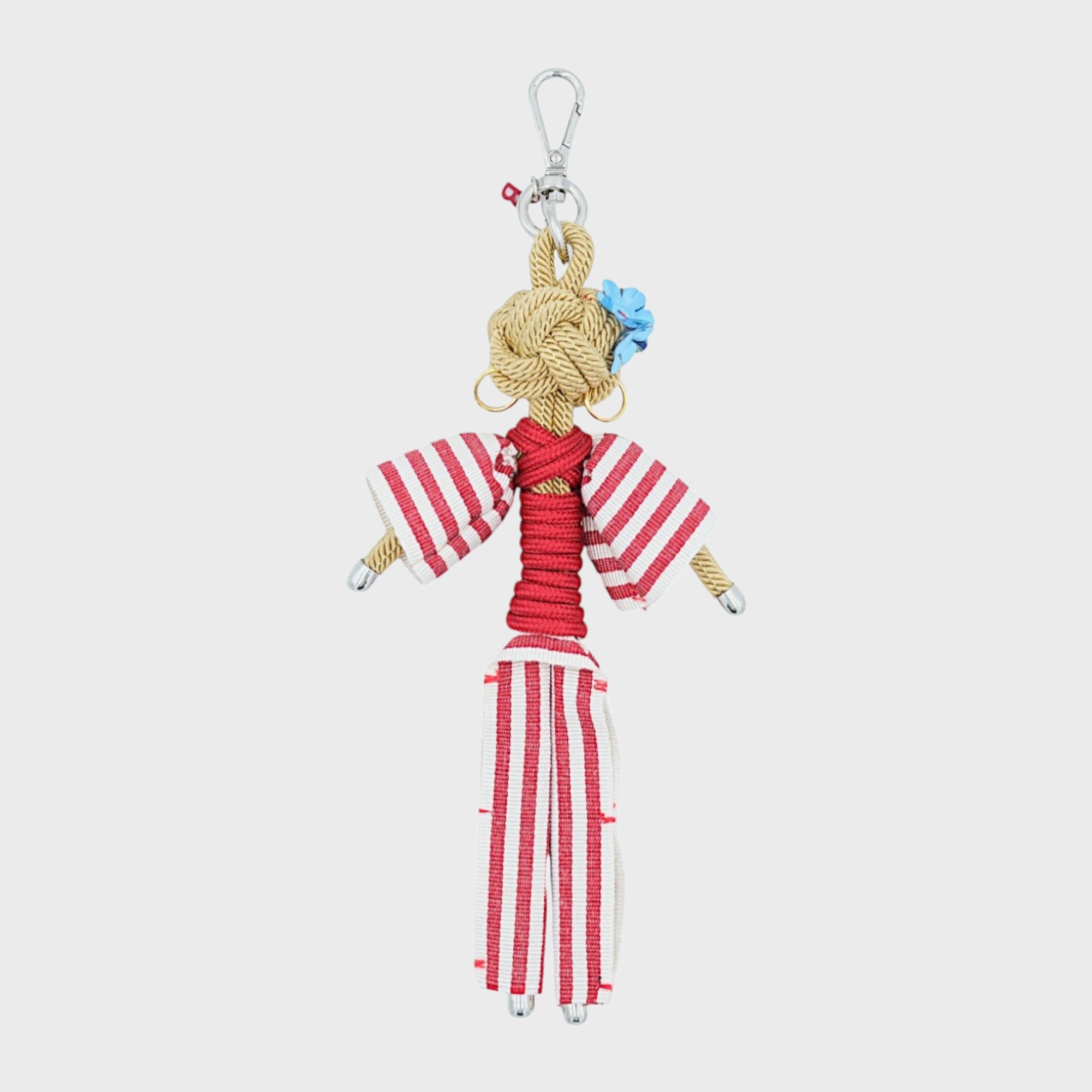 Bag charm featuring a character in a red and white striped overalls, wearing gold hoop earrings and blue flowers behind her ear, all attached to a silver clasp.