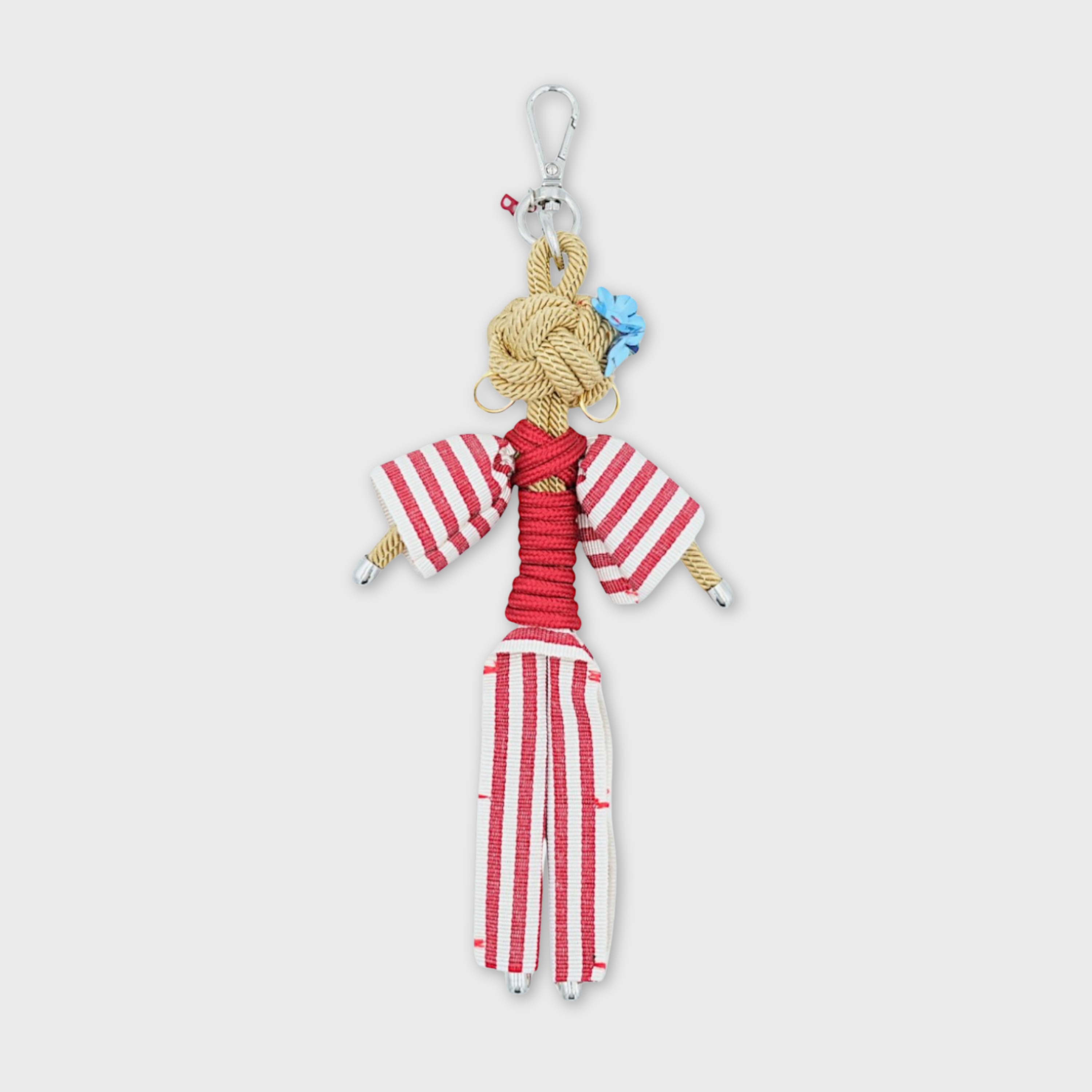 Bag charm featuring a character in a red and white striped overalls, wearing gold hoop earrings and blue flowers behind her ear, all attached to a silver clasp.
