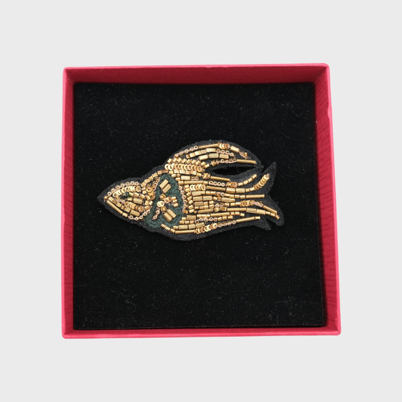 An embroidered brooch representing a golden bird in a box. 