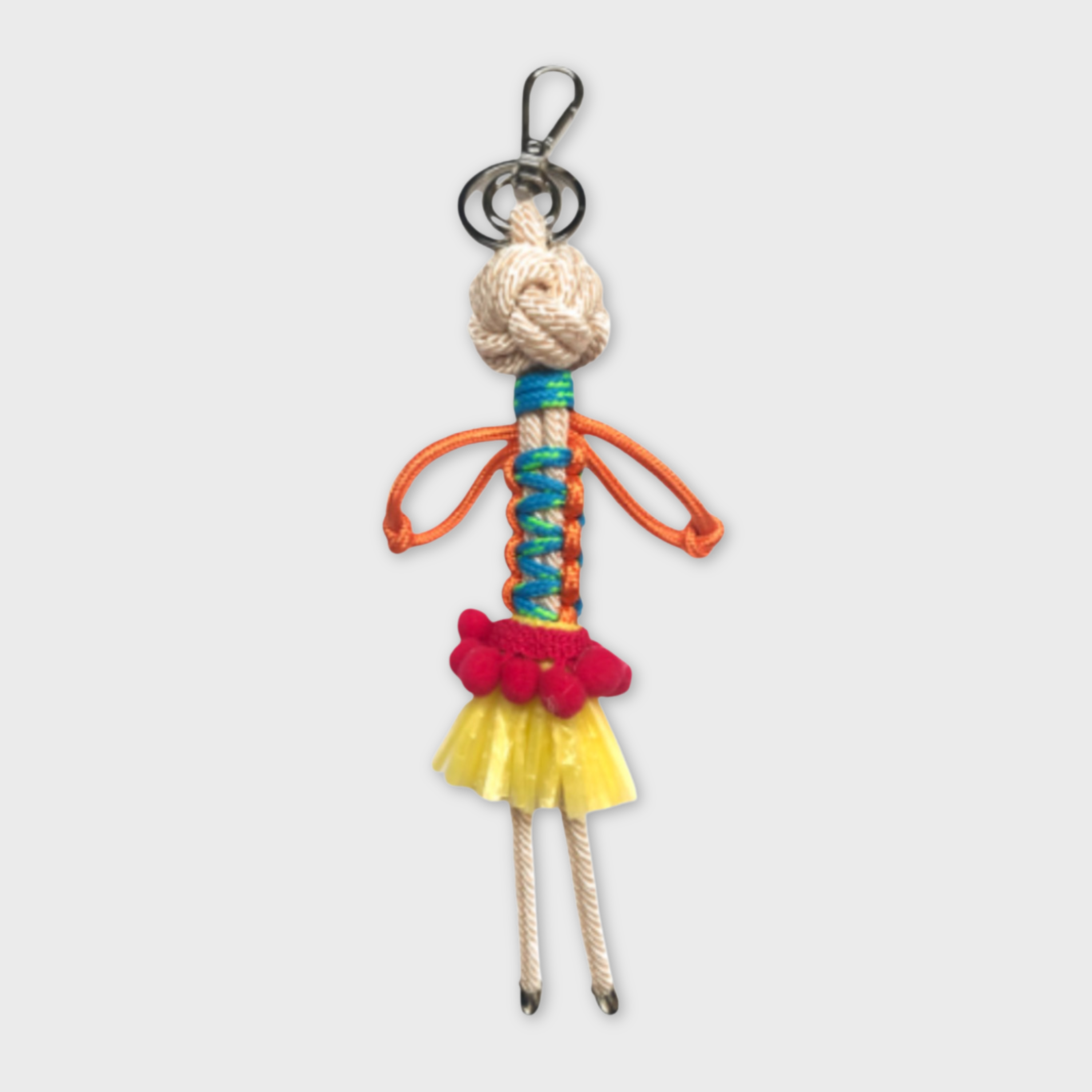 Handmade macramé bag charm featuring an exotic character wearing a short bright yellow skirt and a fun pink belt. She is attached to a silver clasp.