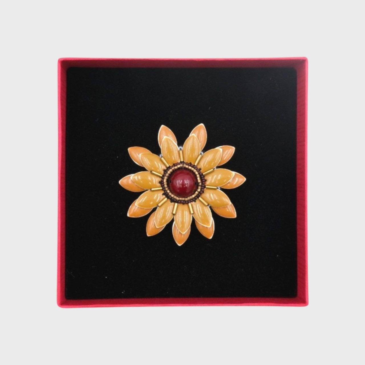 An embroidered brooch representing a beige manuka flower in a box. 