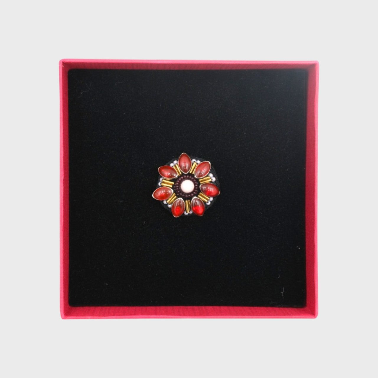 An embroidered brooch representing a red Manuka flower in a box. 