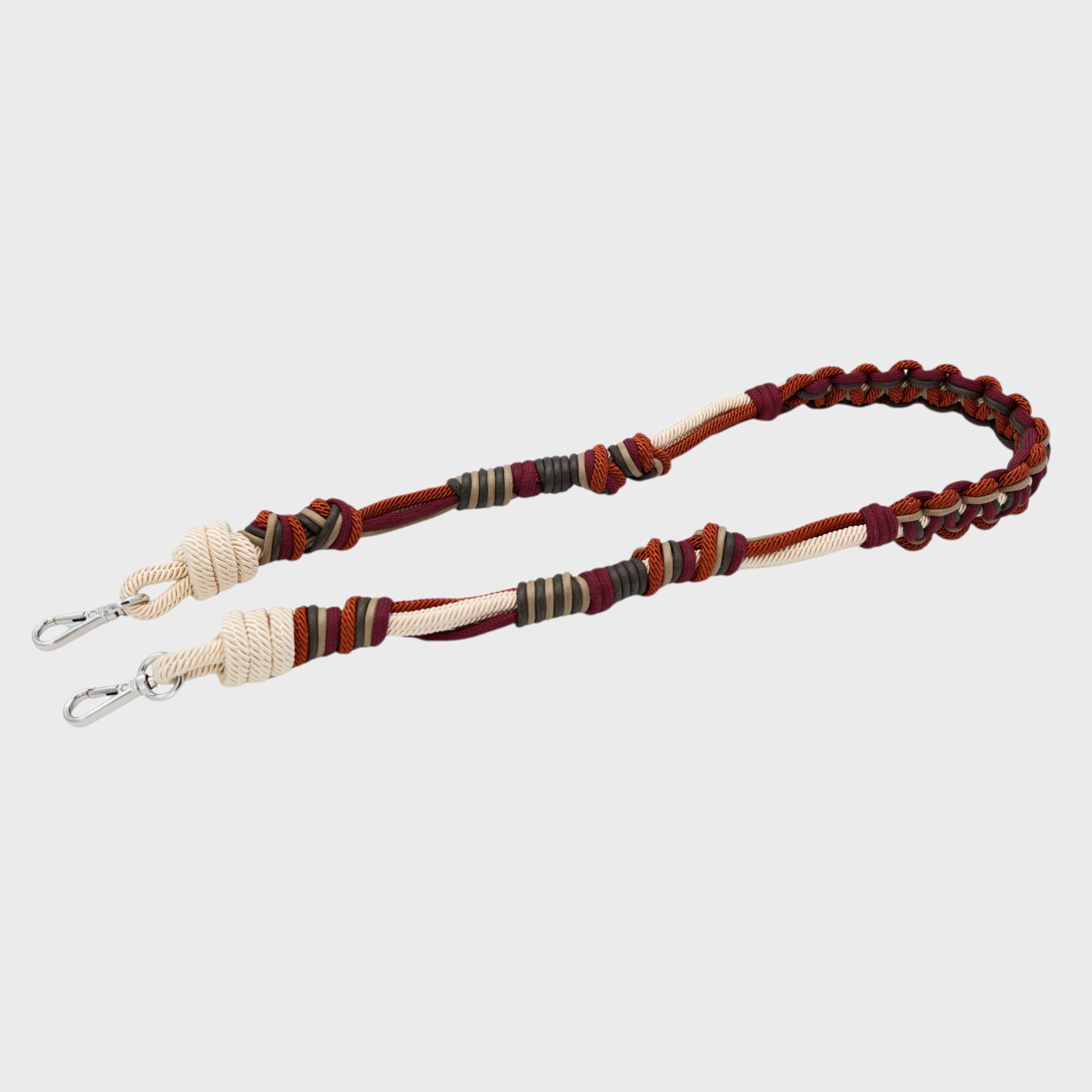 Multicolored braided macramé bag strap in beige, dark red, and dark green with metal hooks on a light gray background.
