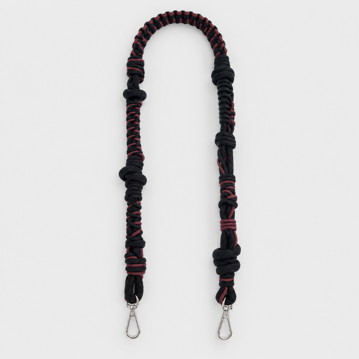 A black and dark red braided macramé bag strap with silver metal snap hooks at the ends, displayed on a clean light gray background.