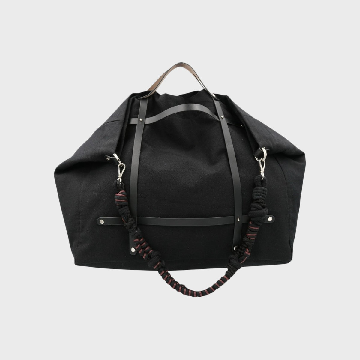 Black duffel bag with a black and red macramé braided bag strap on a light gray background
