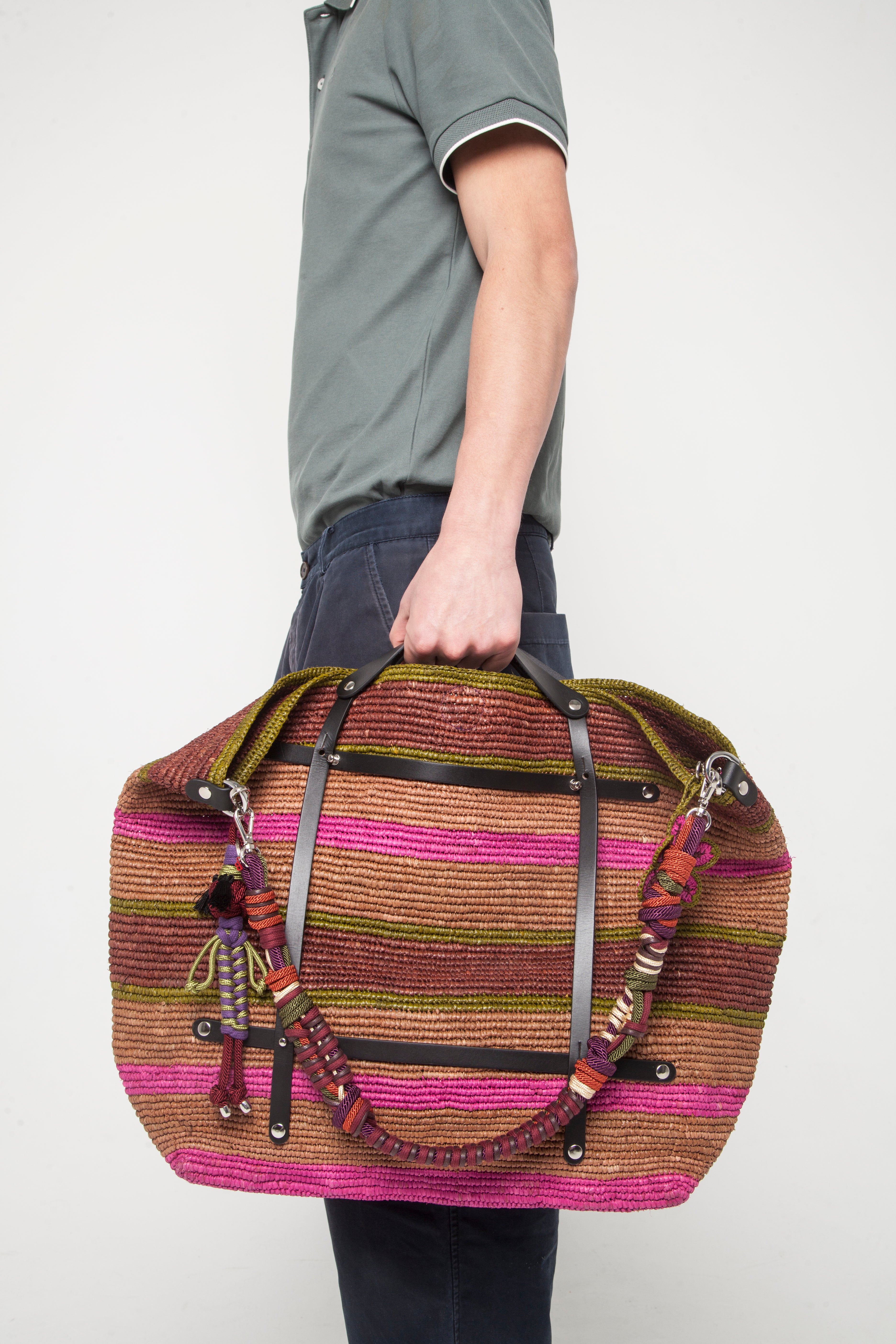 Multicolored braided macramé bag strap in  dark green, purple, and orange, shown on a striped CANDIDE Weekender bag held by a young man.