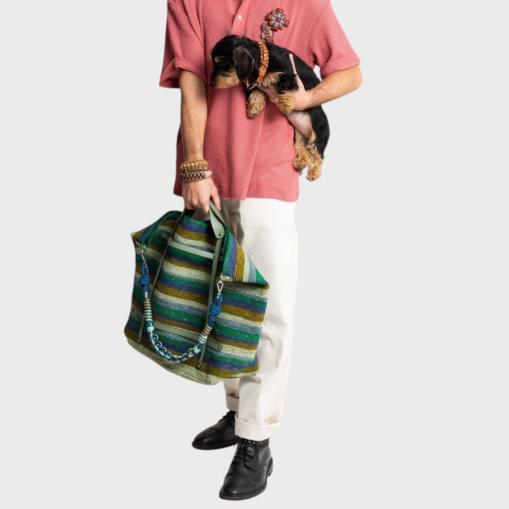 Model carrying the blue and green striped raffia weekend or duffle bag by the green leather strap.