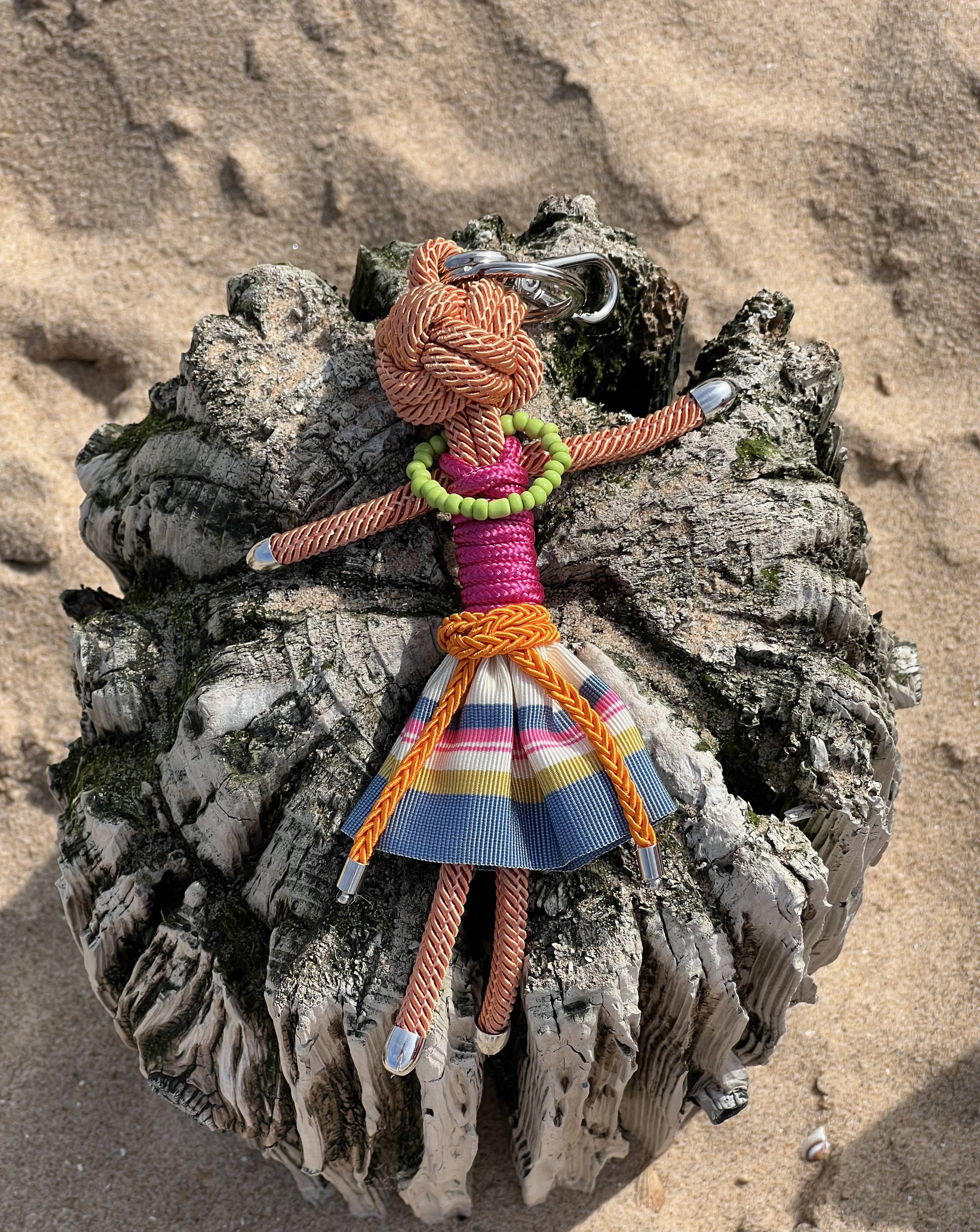 Lola bag charm shown on a sandy beach on a sunny day.